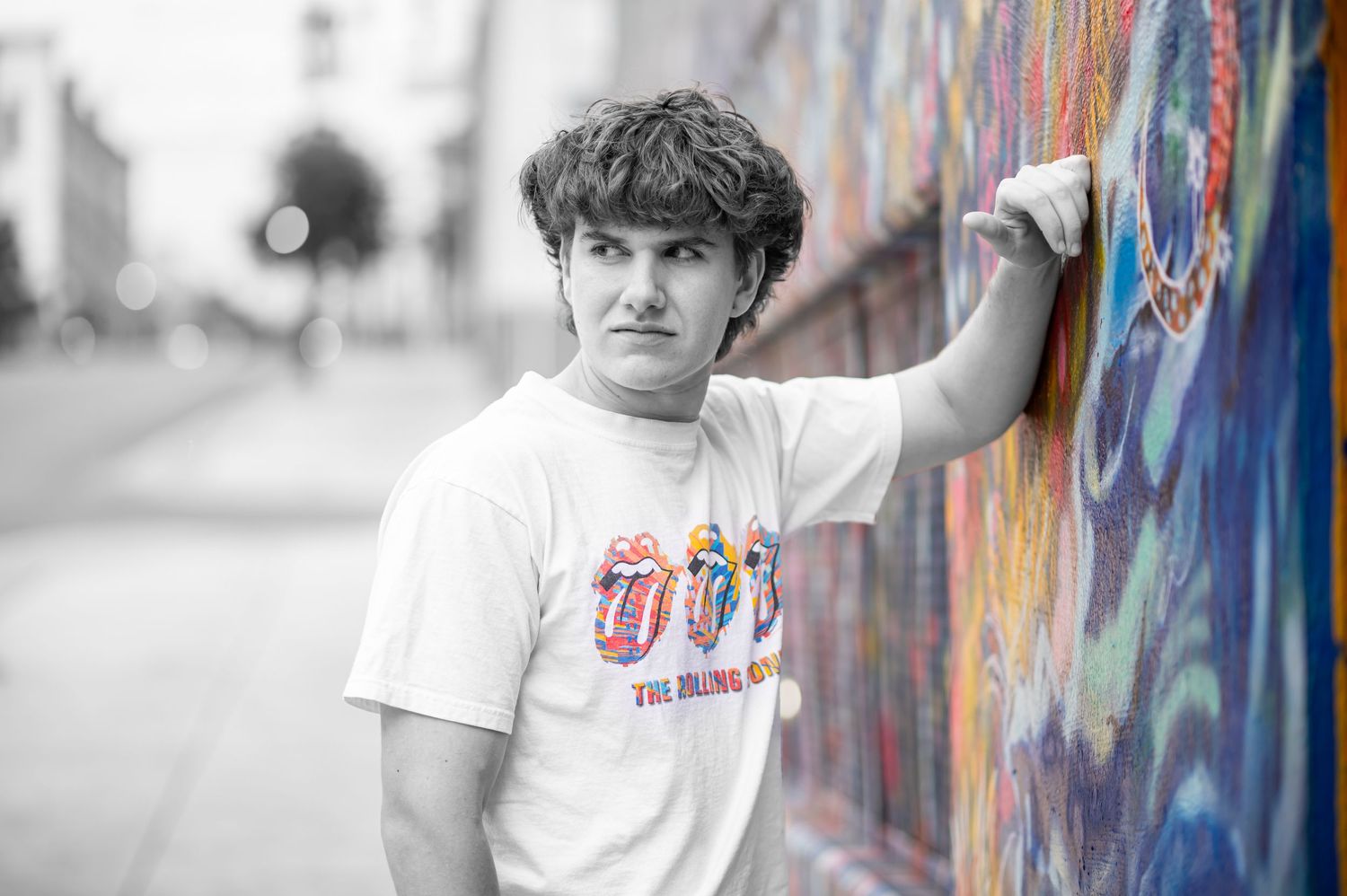 black and white portrait of a young man in a rolling stones tee, leaning his arm against a colorful painted mural in downtown Morgantown, WV