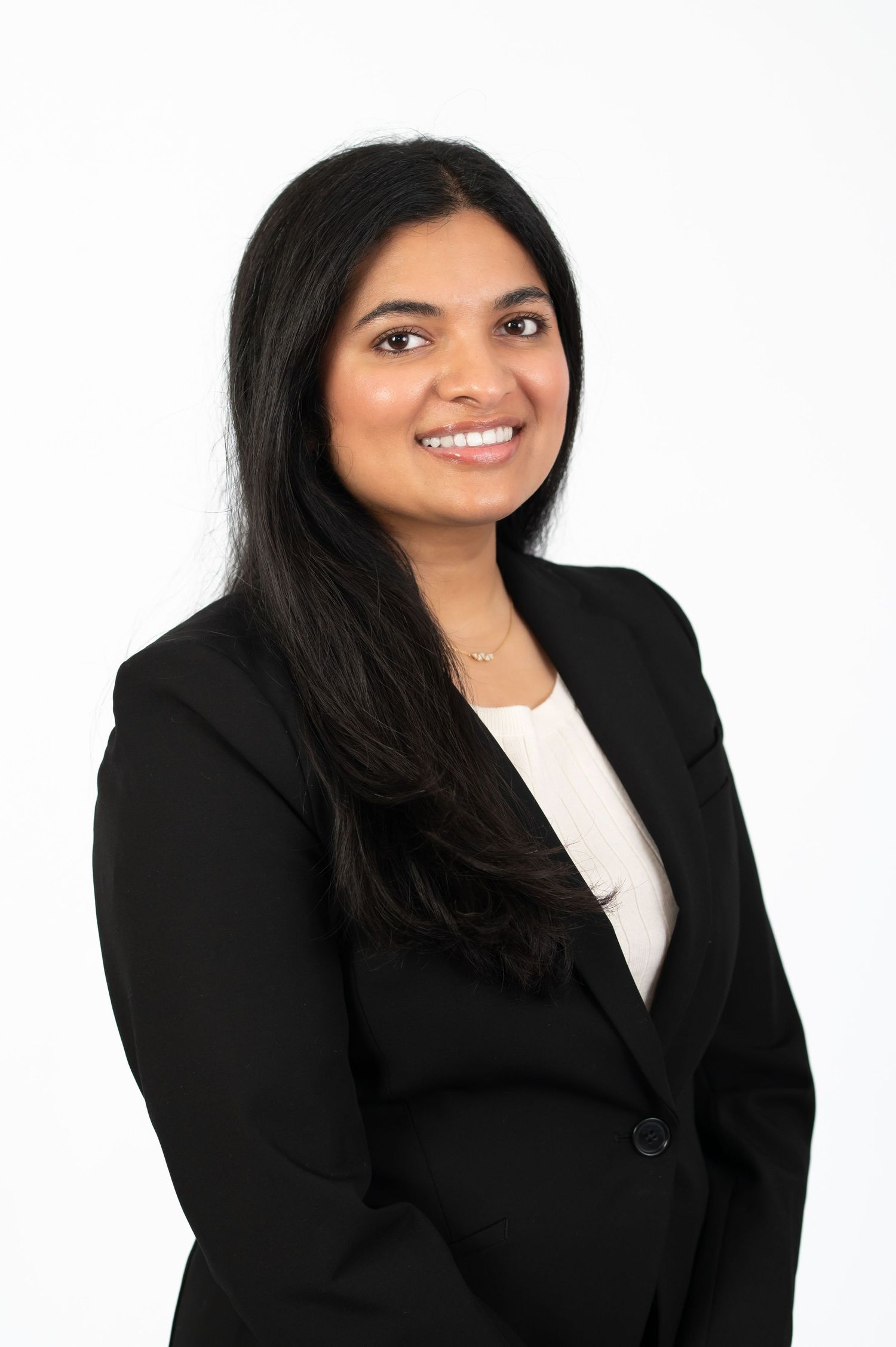 headshot of a young woman with dark hair in a black blazer and white blouse, smiling at the camera, with a bright white background