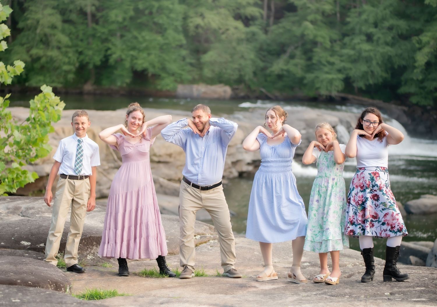 a father and his five teen and young adult children strike a playful silly pose on a large rock in front of the waterfall at Valley Falls