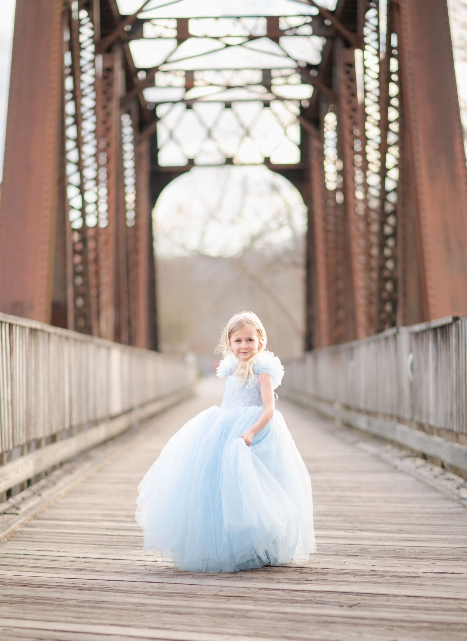 a little girl in a fancy blue dress twirls on an old iron and wood bridge in downtown Morgantown, WV