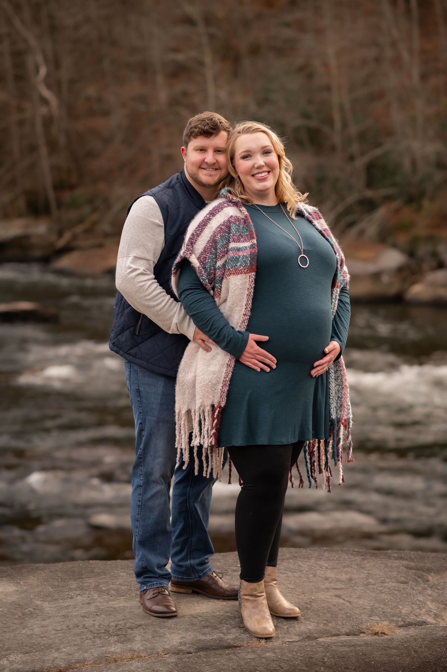 a pregnant couple pose on the rocks in front of the river and falls at Valley Falls State Park in WV