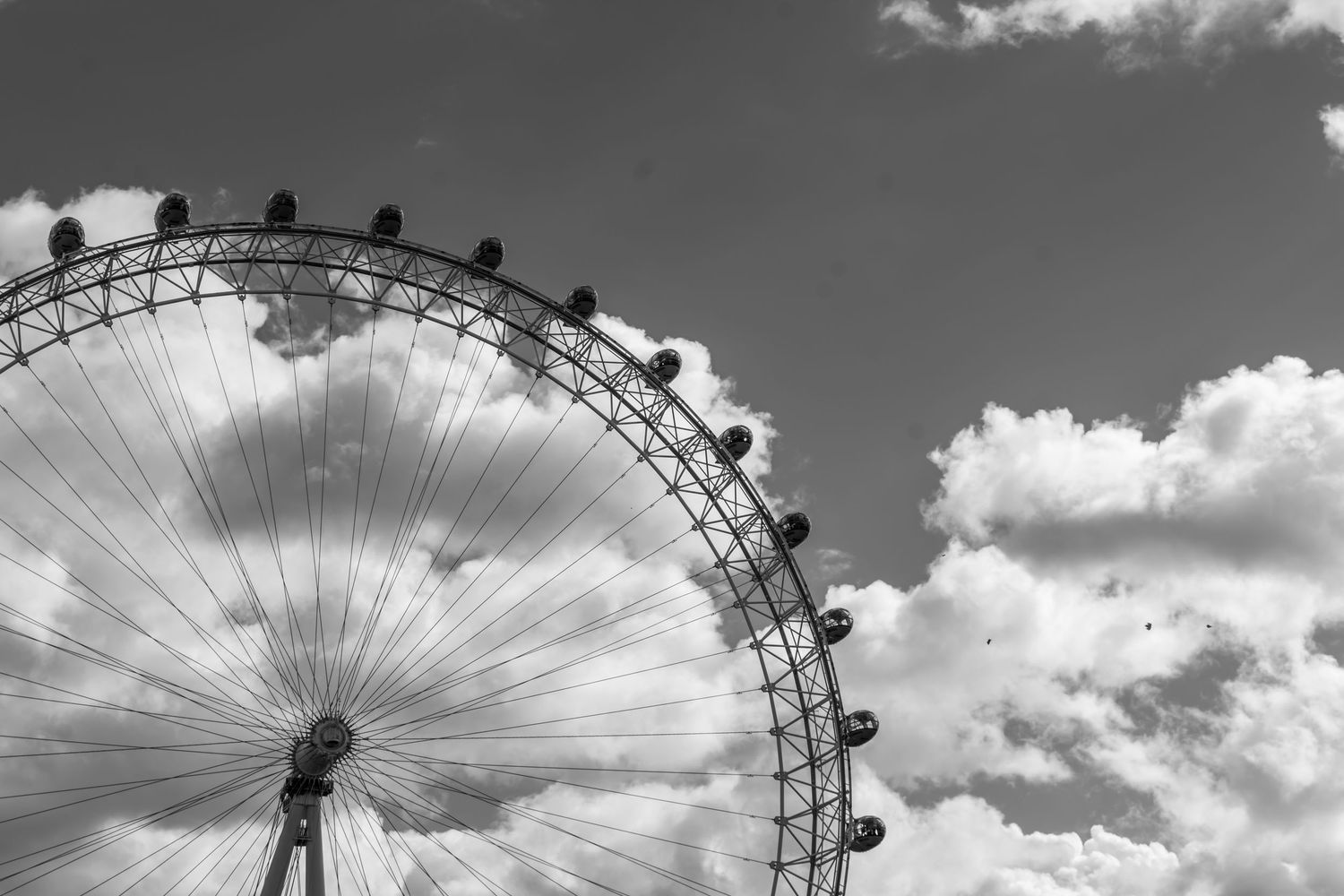Black and white photo of the London Eye Ferris wheel against a cloudy sky.