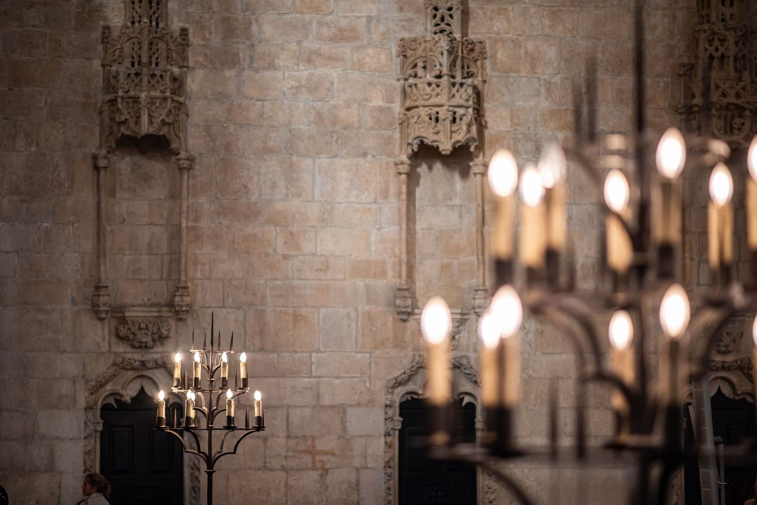 Gothic cathedral interior with ornate stone walls and elegant candelabras glowing with warm candlelight.