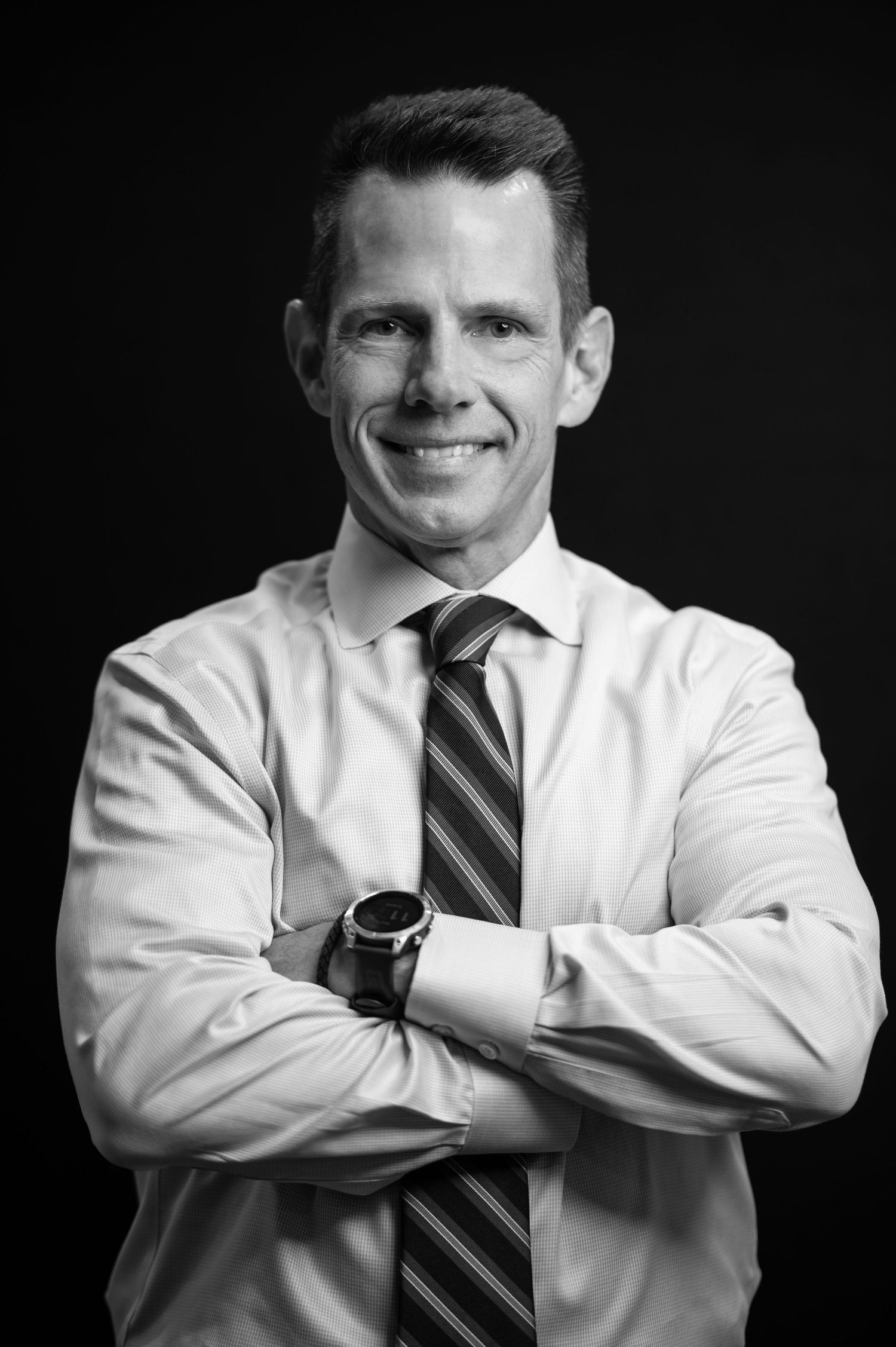a bold, black and white headshot of a male lawyer in a shirt and tie smiling into the camera with arms crossed, against a black background
