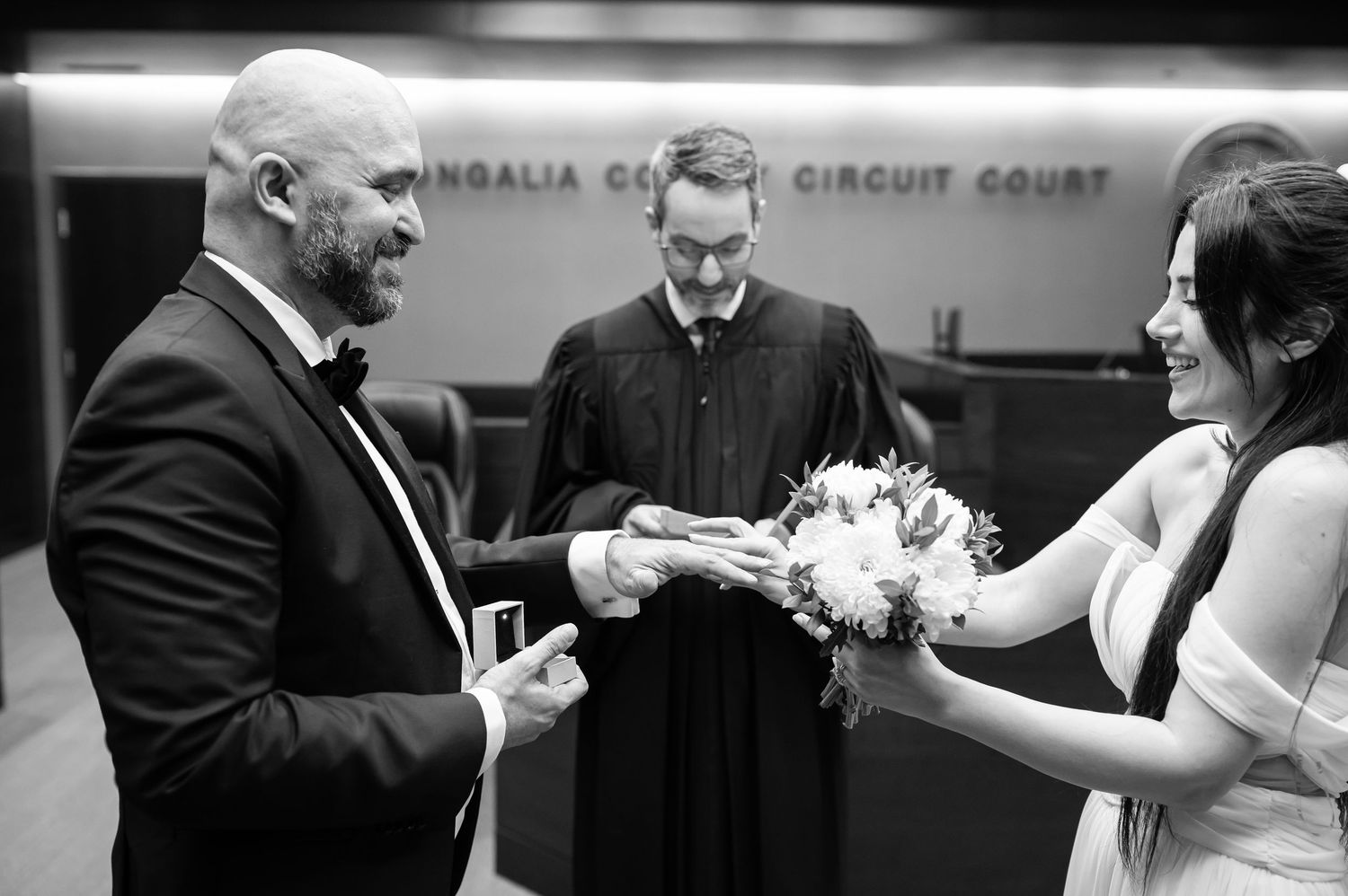 black and white image of the bride, groom, and judge during the ring exchange of a courthouse wedding.