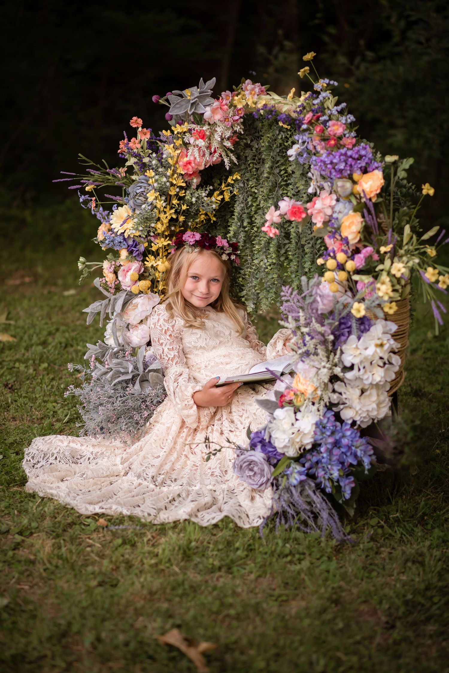a little girl in a white lace dress poses for a portrait in a large archway covered in flowers