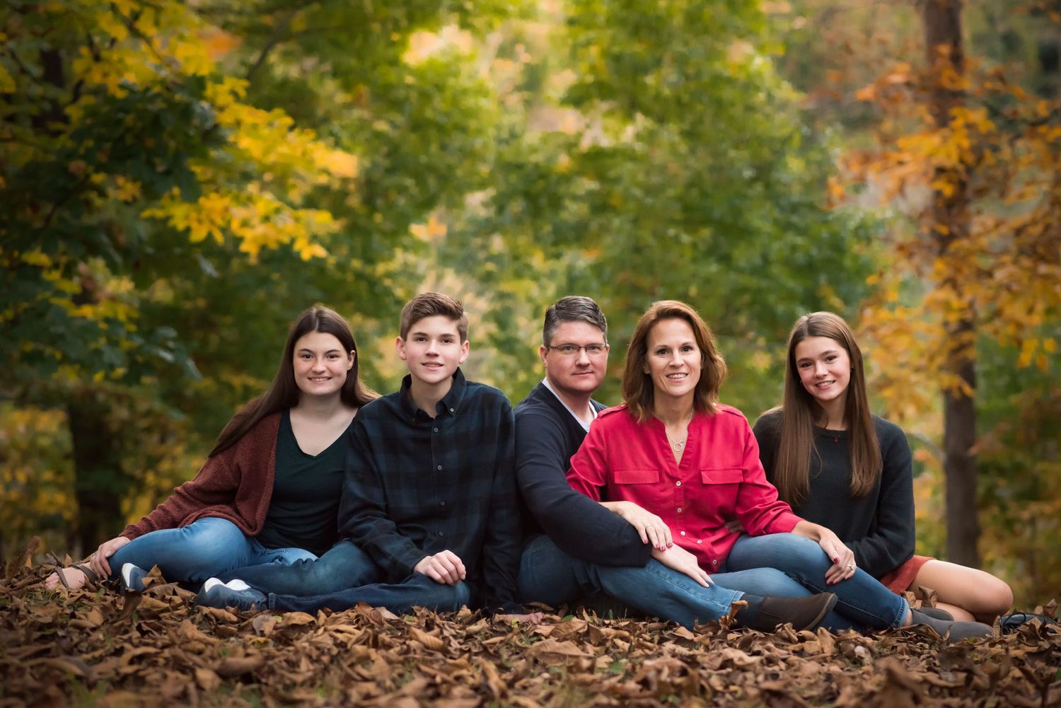 a family of five poses solemnly on the ground with brilliant fall leaves behind them