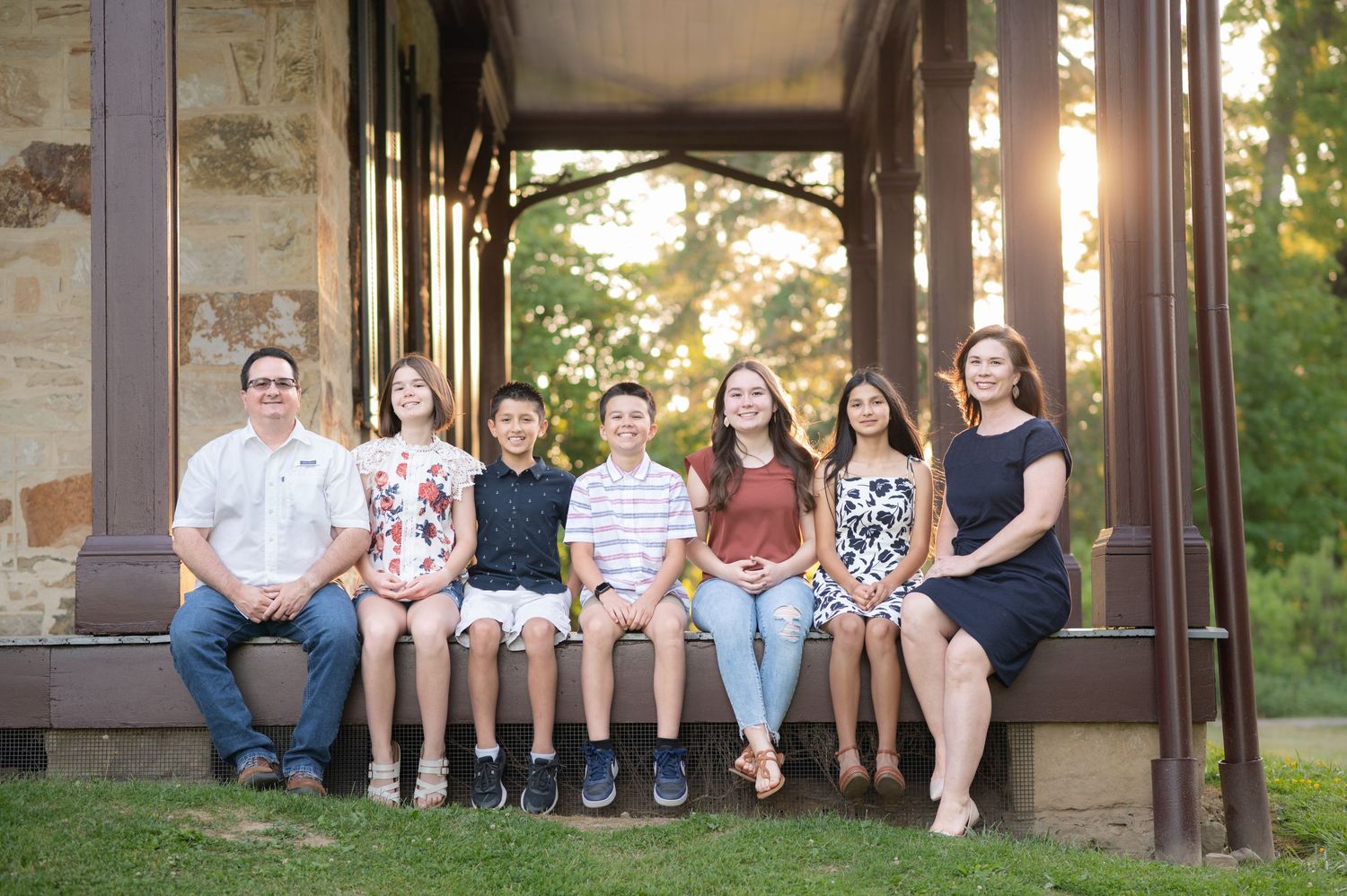 a family of six pose seated side by side on the porch of the Albert Gallatin house in Point Marion, PA, with the sun shining behind them