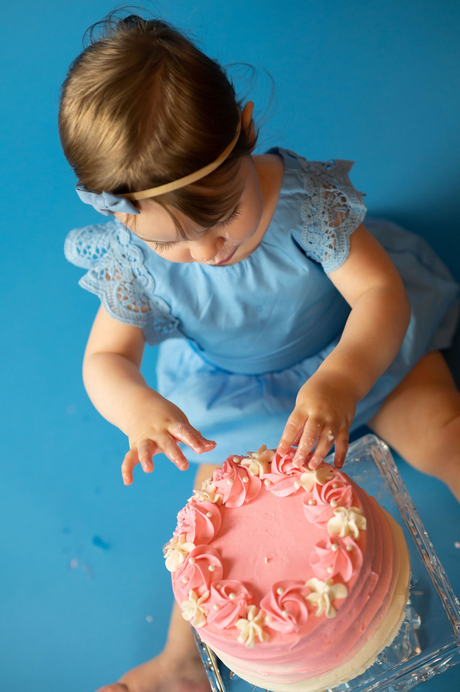 a little girl in blue sits on a blue background with her pink smash cake
