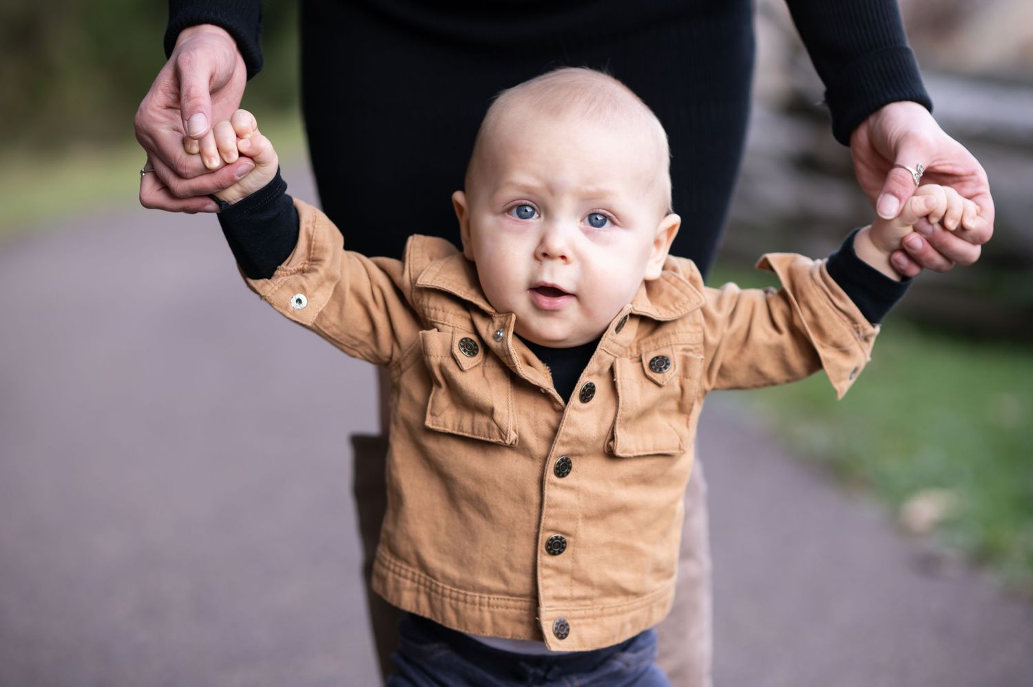 closeup of a blonde, blue eyed toddler boy holding his parents' hands