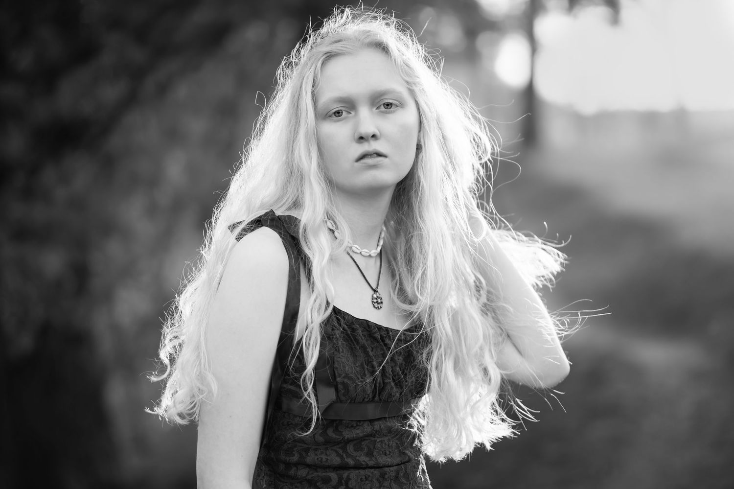 Black and white closeup senior portrait of a beautiful blonde high school student in a black dress with the sun lighting up her hair