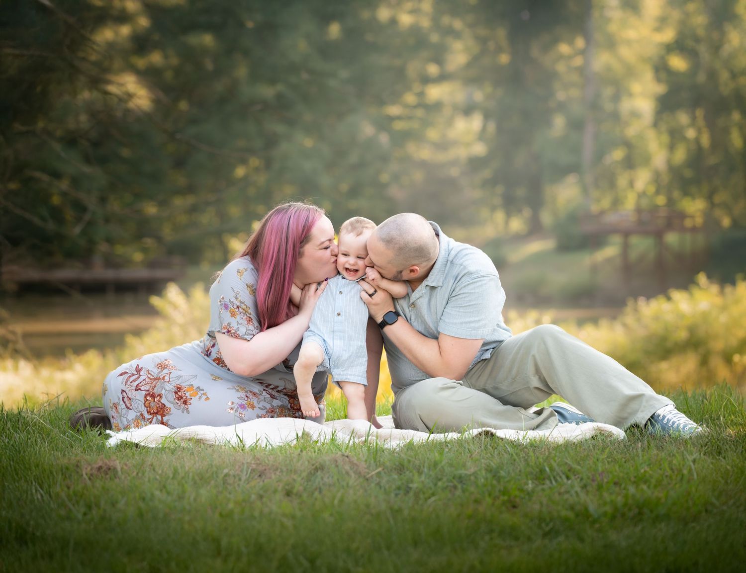 a young couple sit on a blanket in the grass with their toddler son, and kiss his cheeks as he laughs; shot in Morgantown, WV