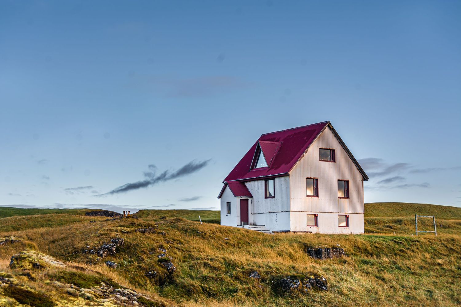 White house with red roof on grassy hill under blue sky in Iceland.