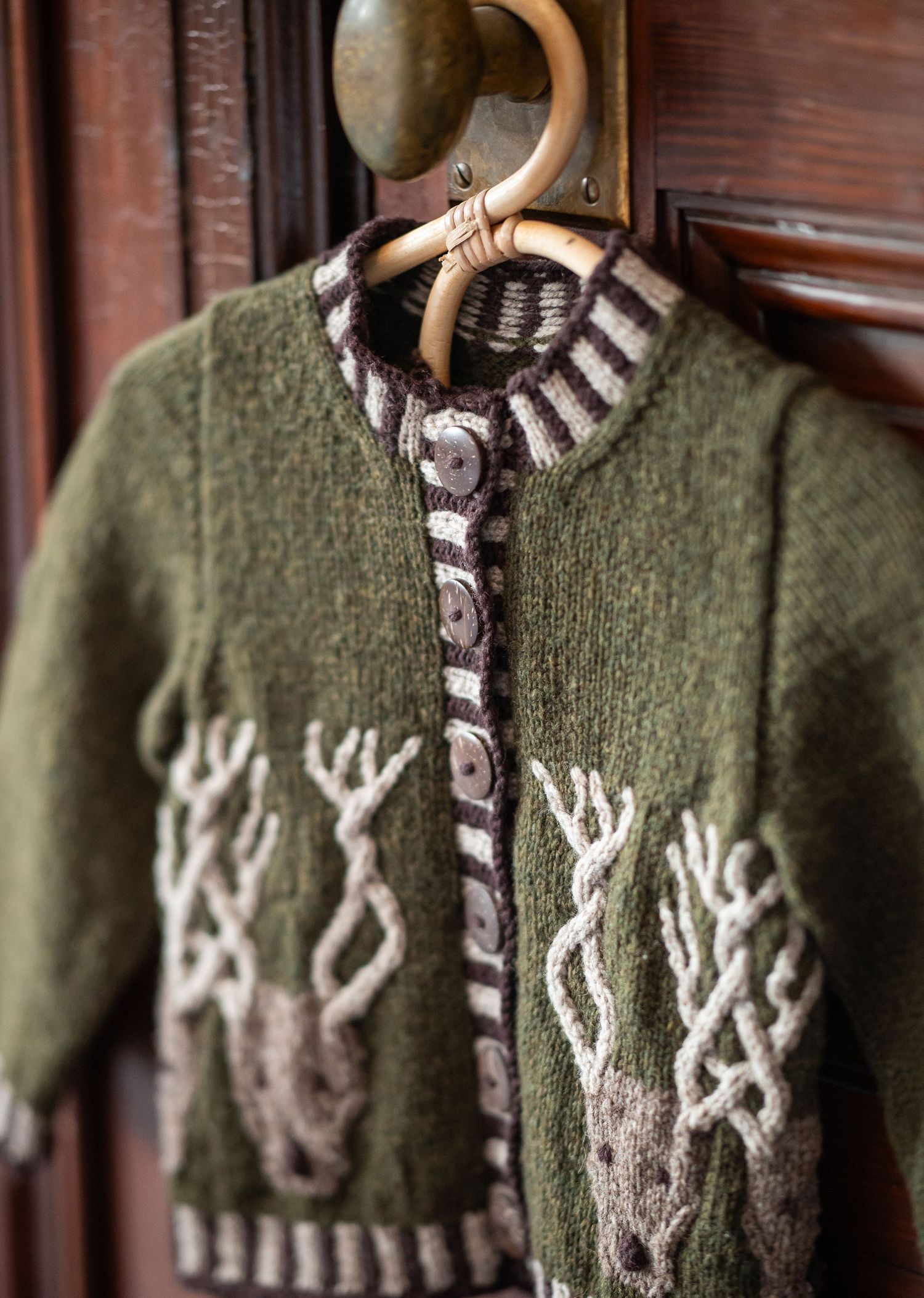 Green knitted cardigan with reindeer pattern and brown buttons on wooden hanger by local artisan Melanie Rountree