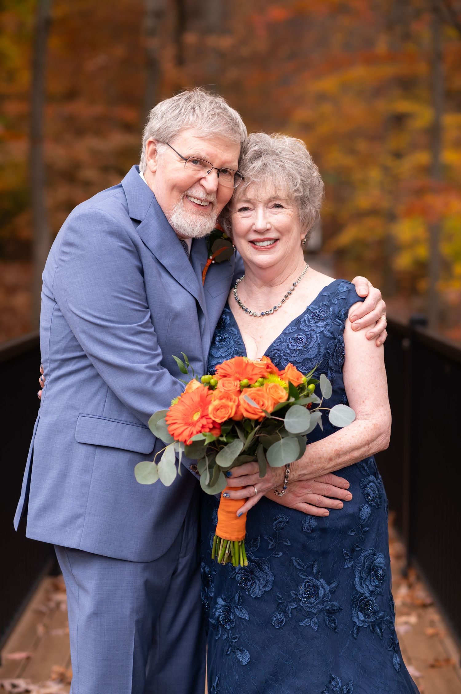 Closeup wedding portrait of an older couple smiling and holding each other close, with autumn leaves in the background at the Botanic Garden