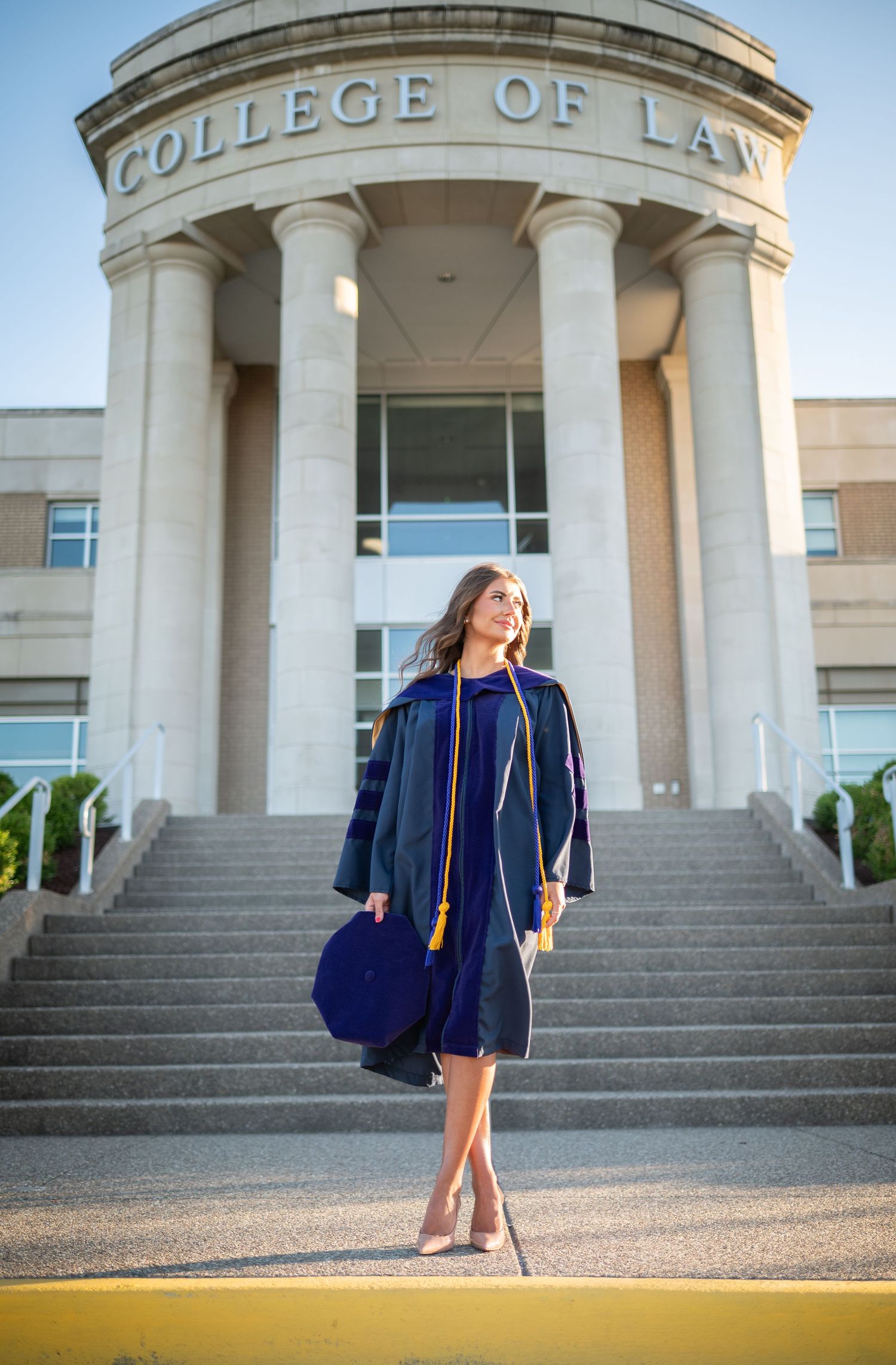 a law school graduate in her blue WVU cap and gown stands in front of the law school