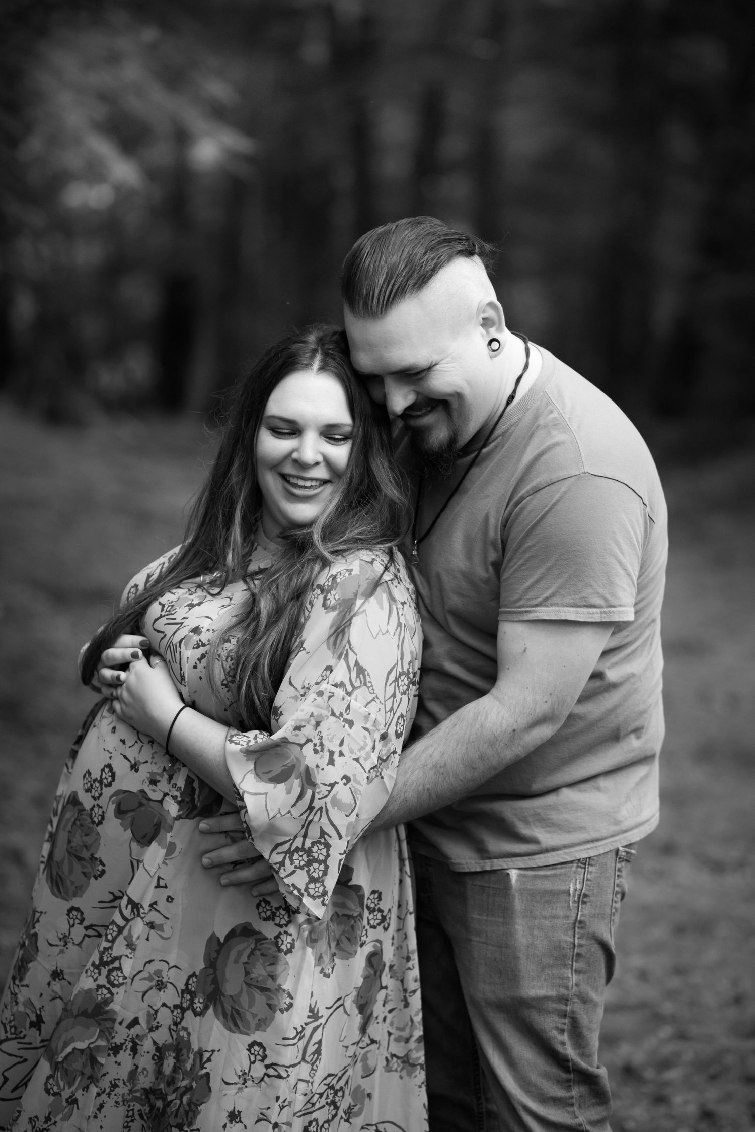 black and white portrait of a pregnant woman and her husband standing together and laughing