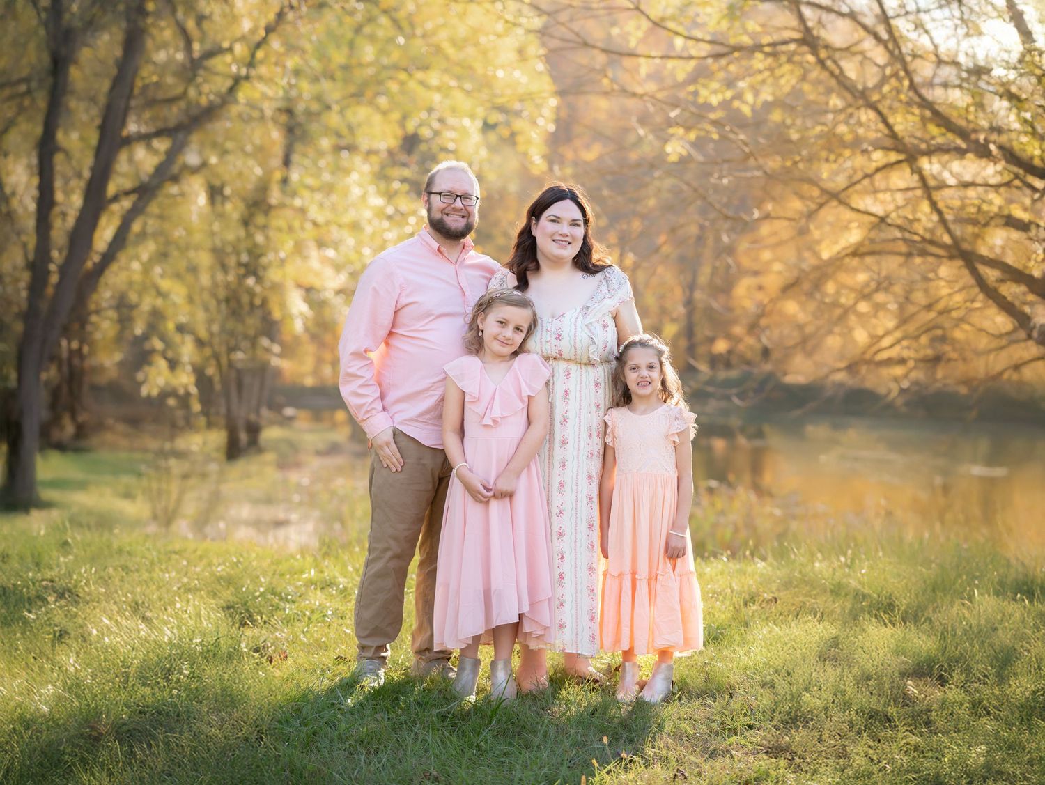 a family of four in pink and white poses for an autumn portrait with brilliant orange and yellow foliage behind them, in Morgantown WV