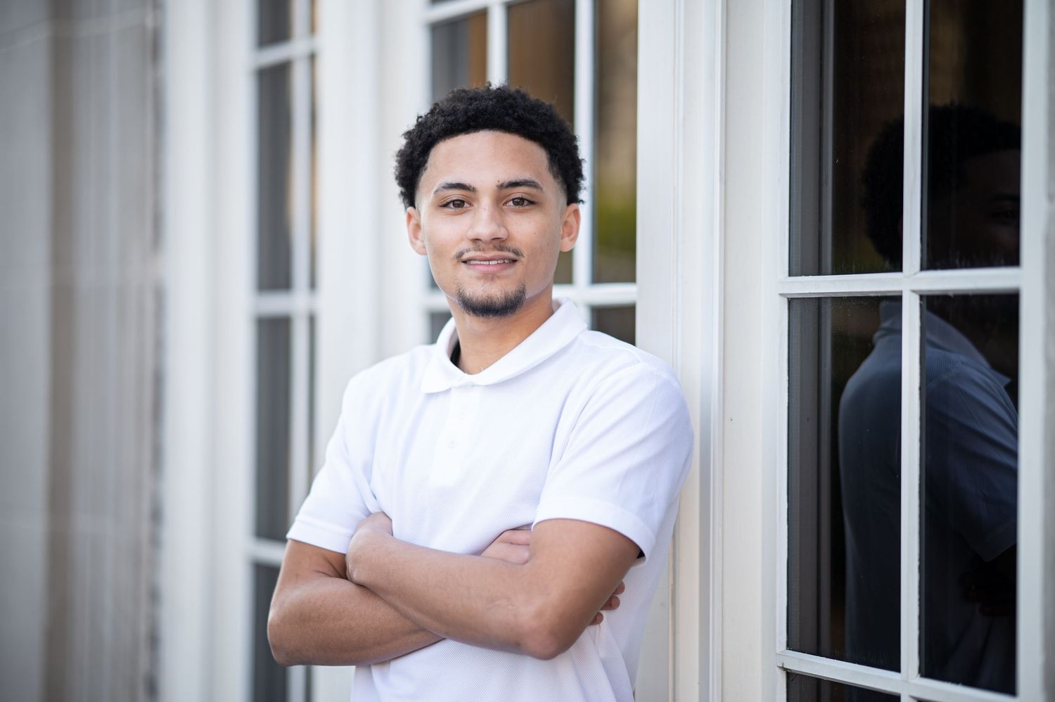 a high school graduate in a white shirt poses for a senior portrait in front of white framed window in downtown Morgantown