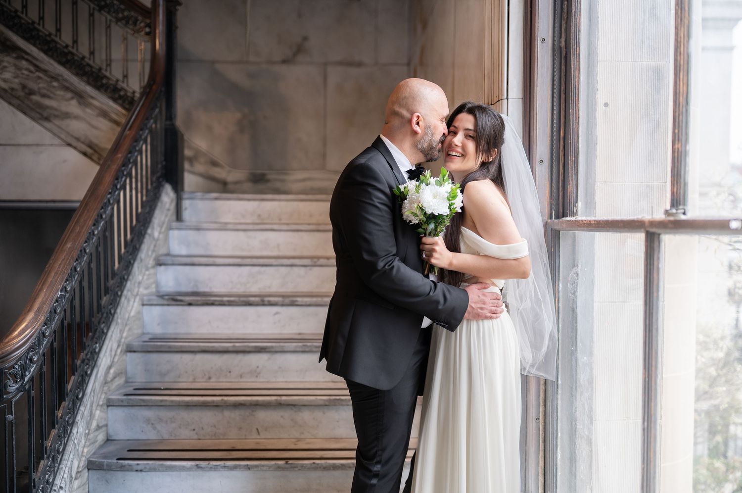 a bride and groom pose for a portrait on a marble staircase with ornate wrought iron railings after a courthouse elopement in morgantown, wv