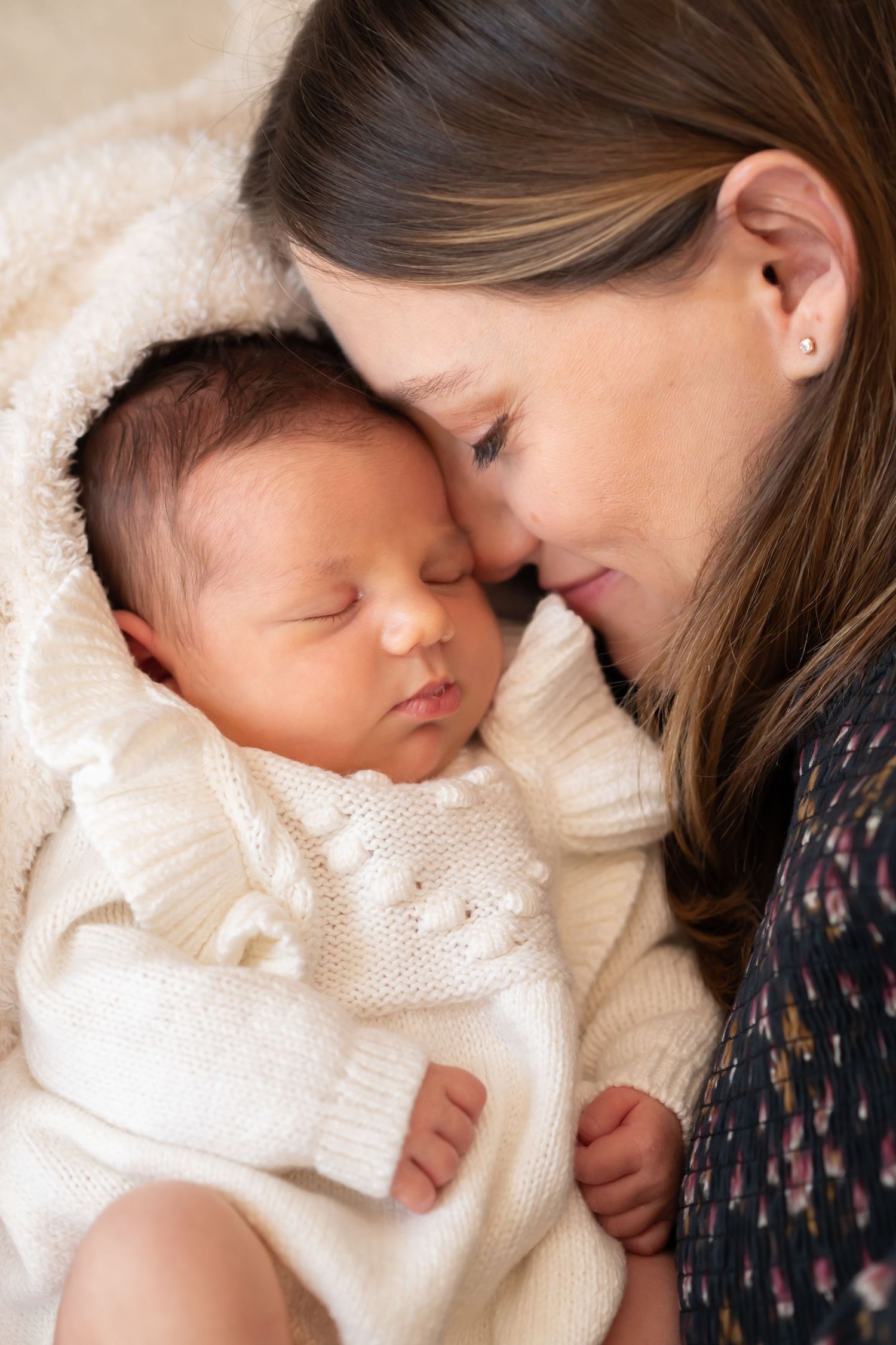 Sweet closeup newborn family portrait of a mother in a black dress, nestled close to her new baby wrapped in a cream sweater dress