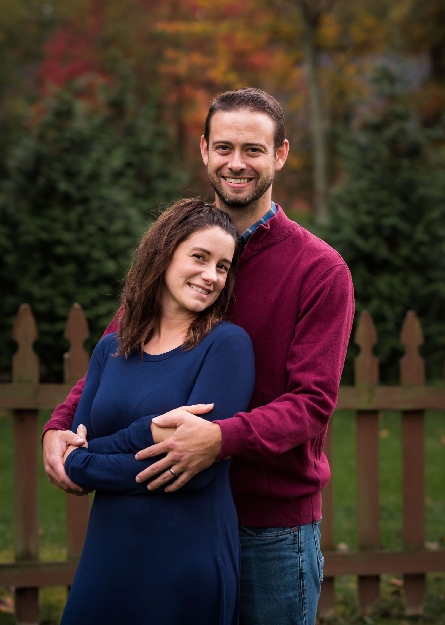a beautiful couple in dark sweaters embrace and smile at the camera for an outdoor portrait at their home in Morgantown, WV