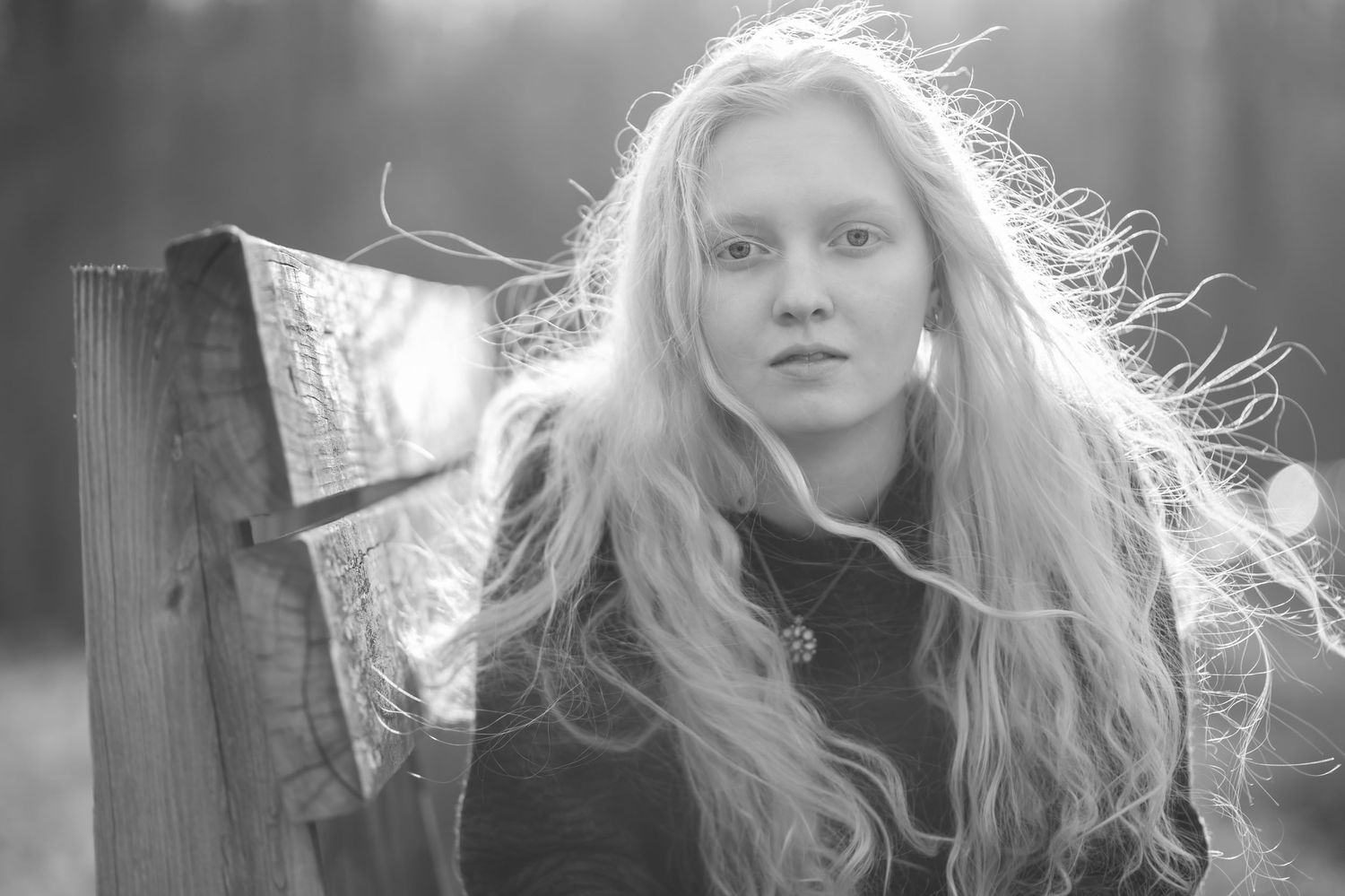 vogue black and white portrait of a young woman on a park bench with the wind blowing her long wavy blonde hair