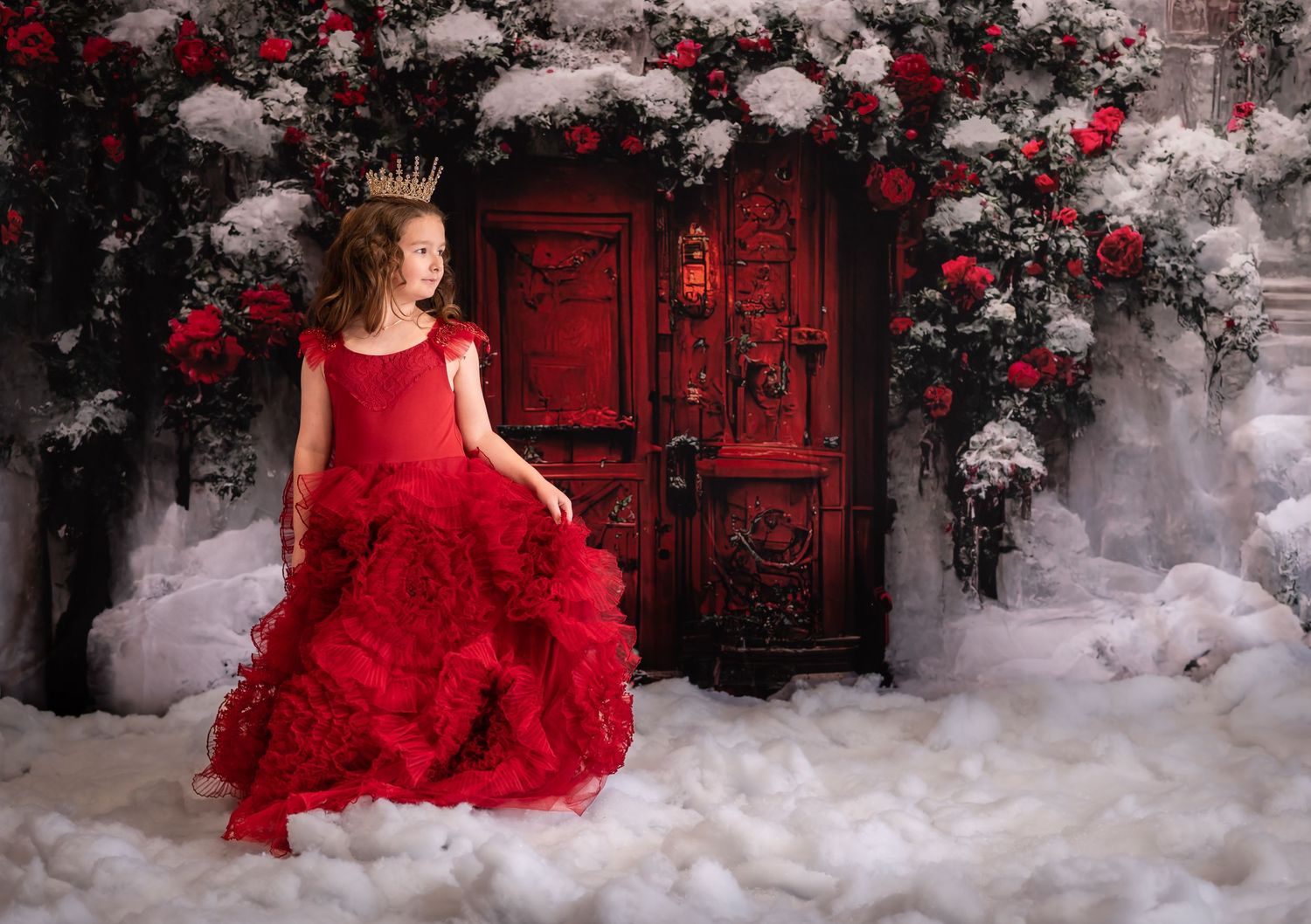 a little girl in a fancy red gown twirls in the snow with a bright red door in the background