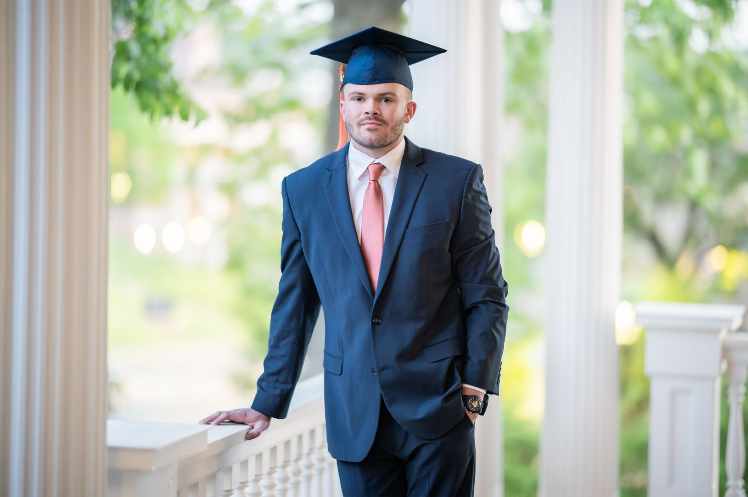 A WVU graduate in a blue suit and red tie poses for a portrait in his graduation cap in Morgantown, WV