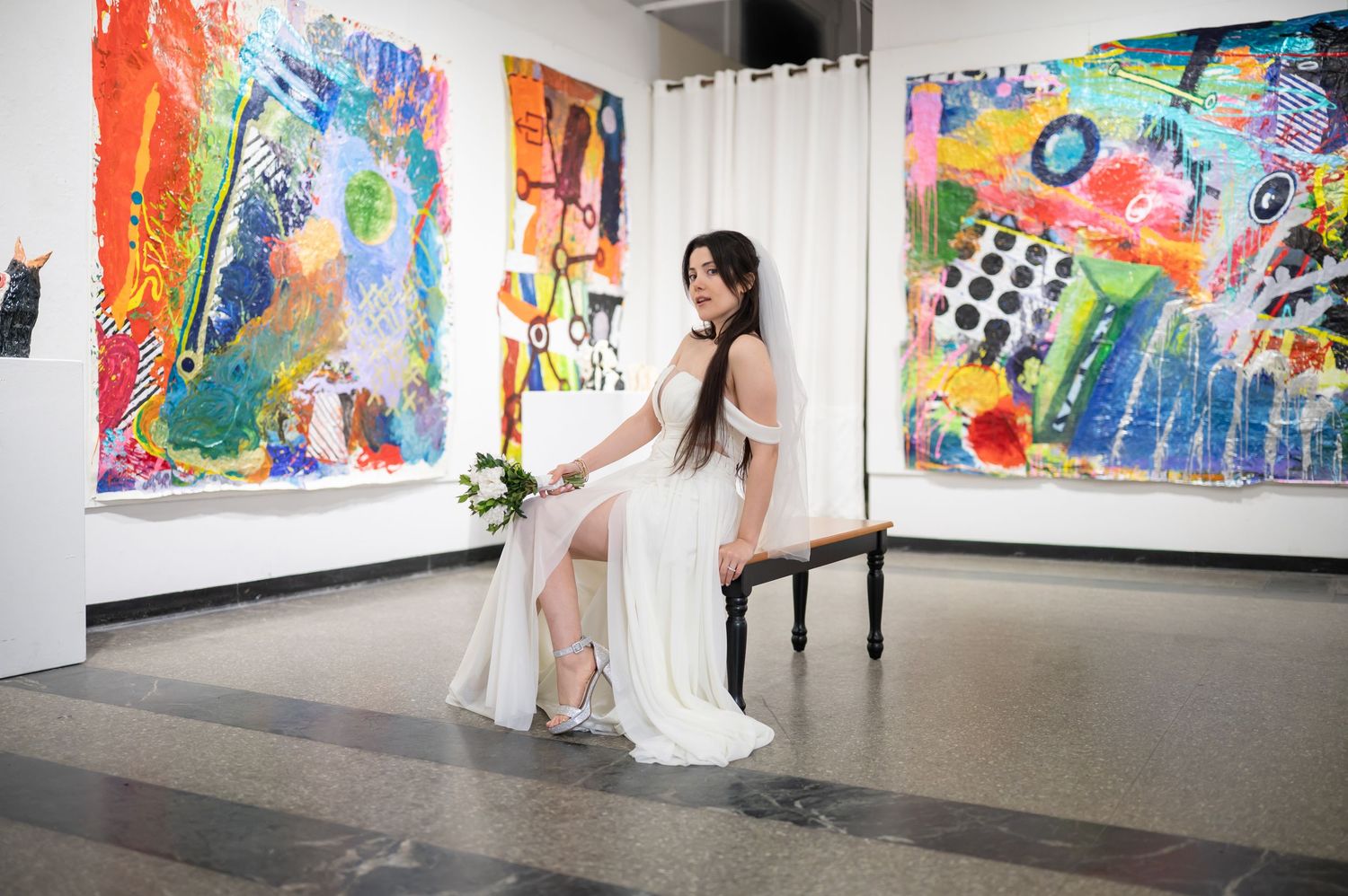 a bride in a modern white wedding gown poses for a portrait in an art gallery surrounded by bright abstract art pieces in Morgantown, WV