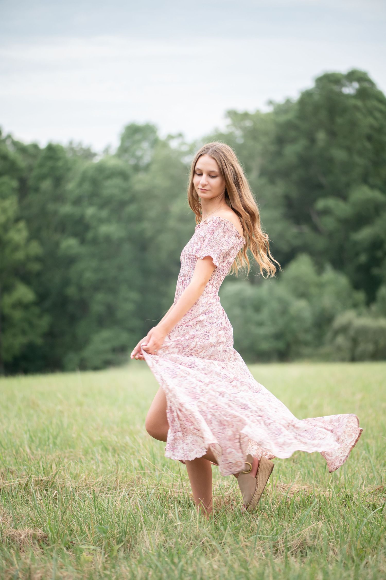 a young woman in a pale pink dress twirls for a senior portrait in a large field with trees in the background, just outside Pt. Marion, PA