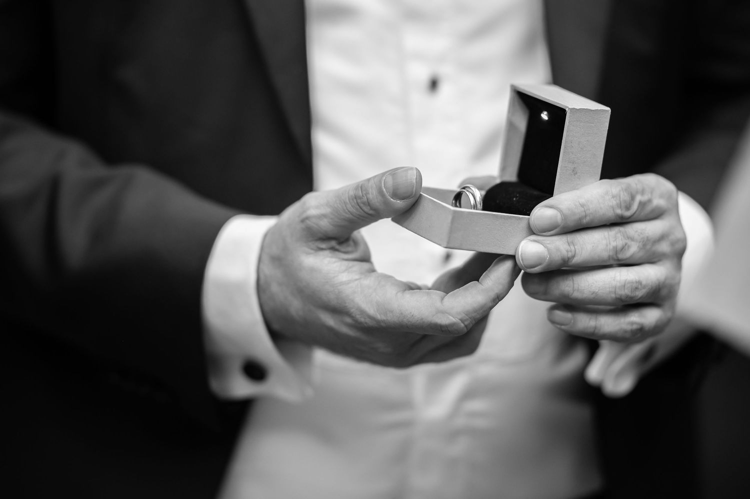 closeup of a groom's hands holding an open wedding ring box