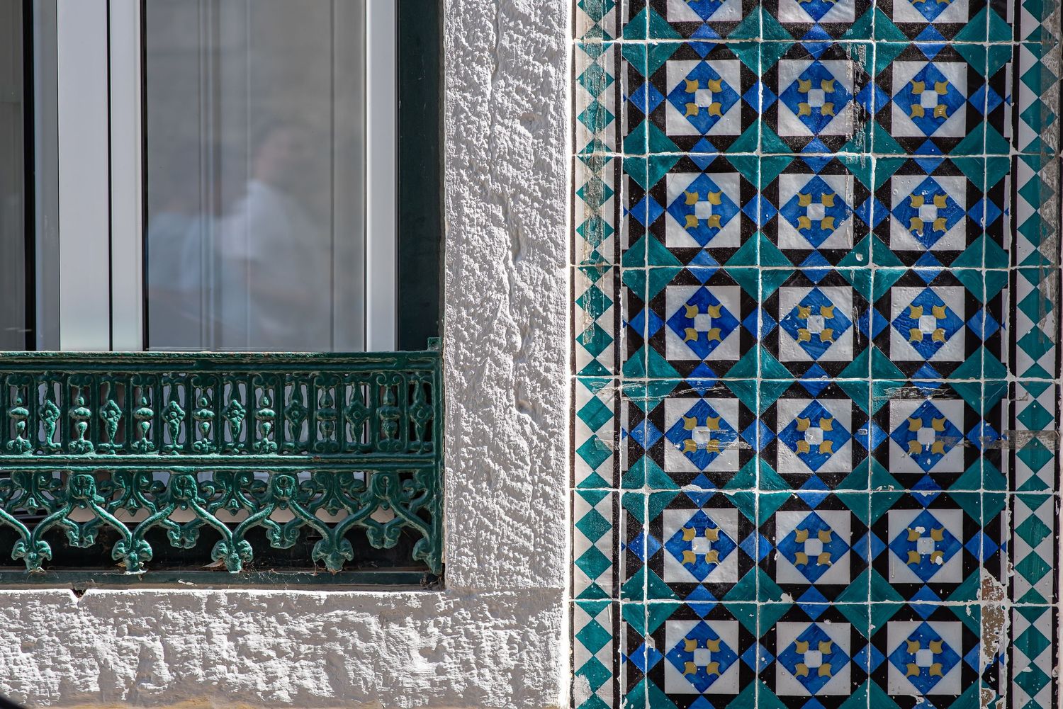 Close-up of a building facade with decorative blue and green azulejo tiles and ornate green ironwork window trim.