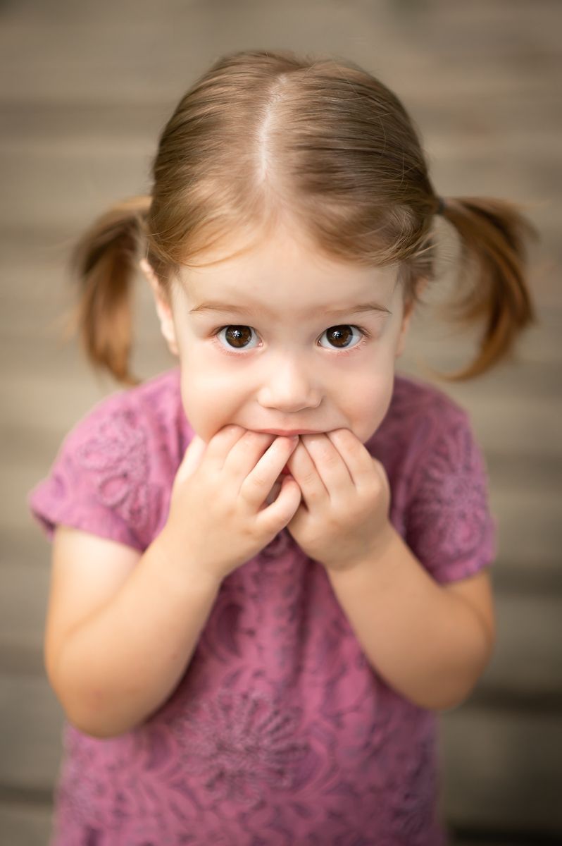 a sweet little girl in a pink dress with pigtails looks innocently up at the camera with big brown eyes
