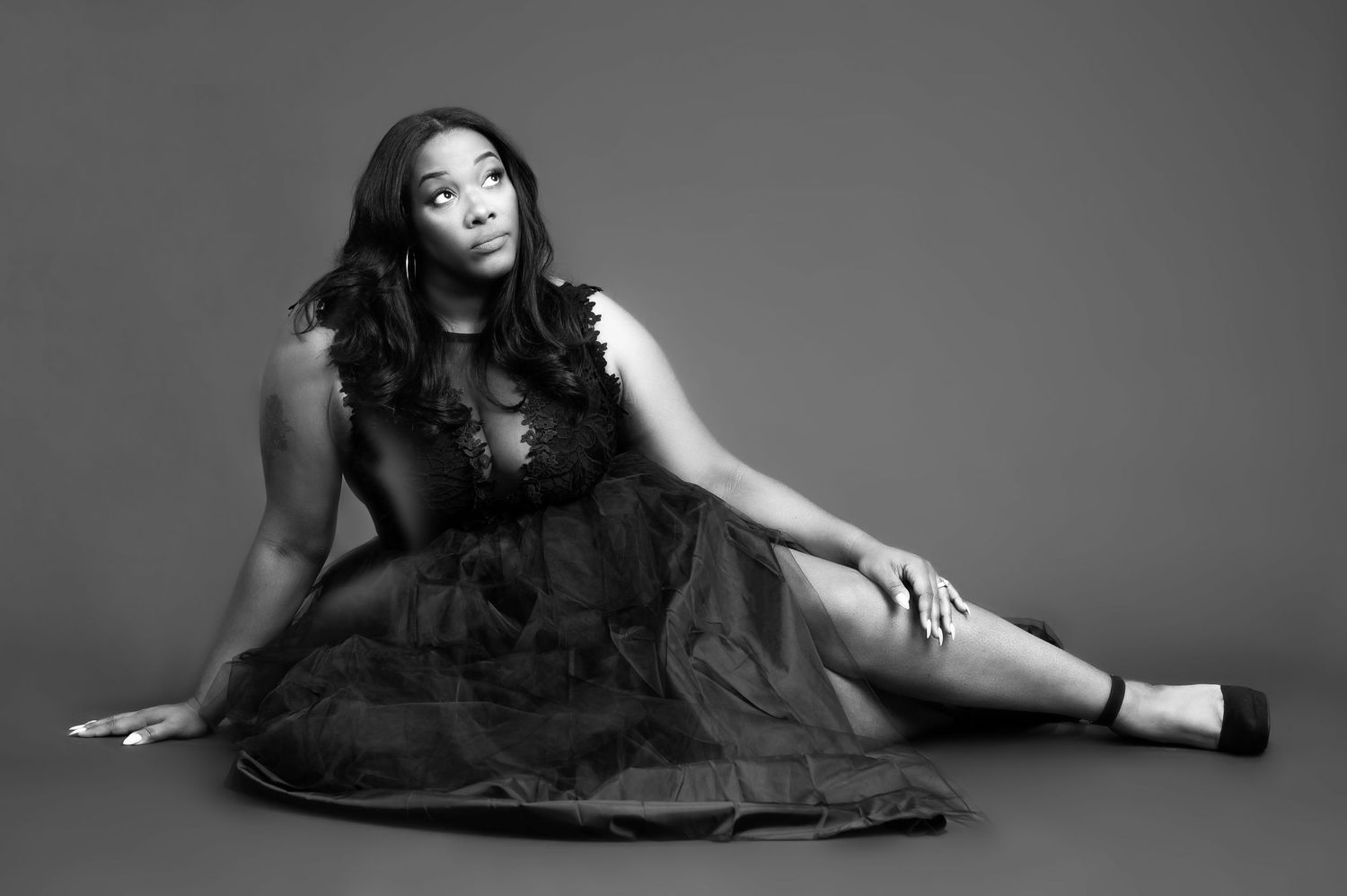 female empowerment portrait of a beautiful black woman in a fancy black dress, seated on a gray studio background
