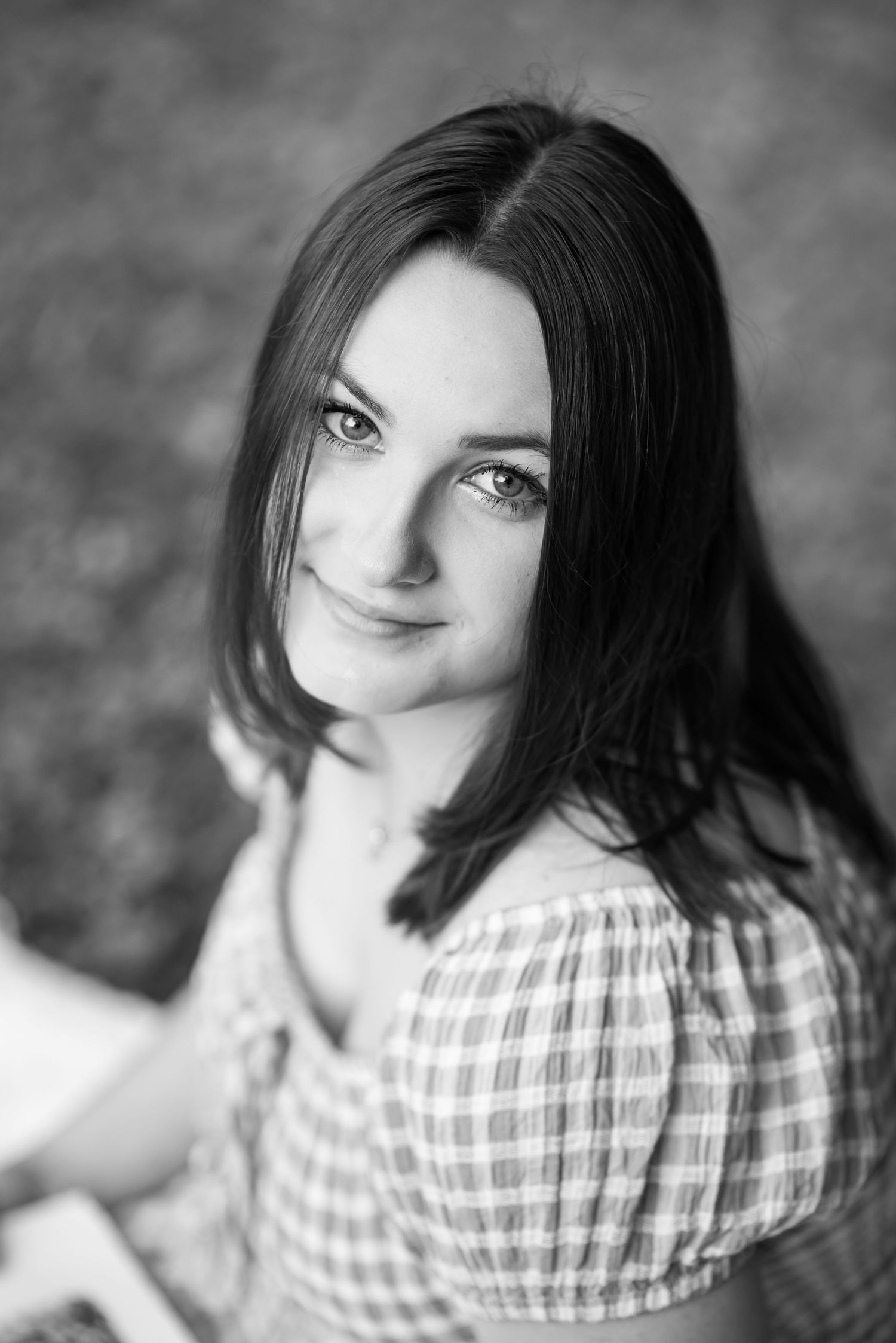 closeup black and white portrait of a dark haired young woman in a gingham dress, smiling up at the camera