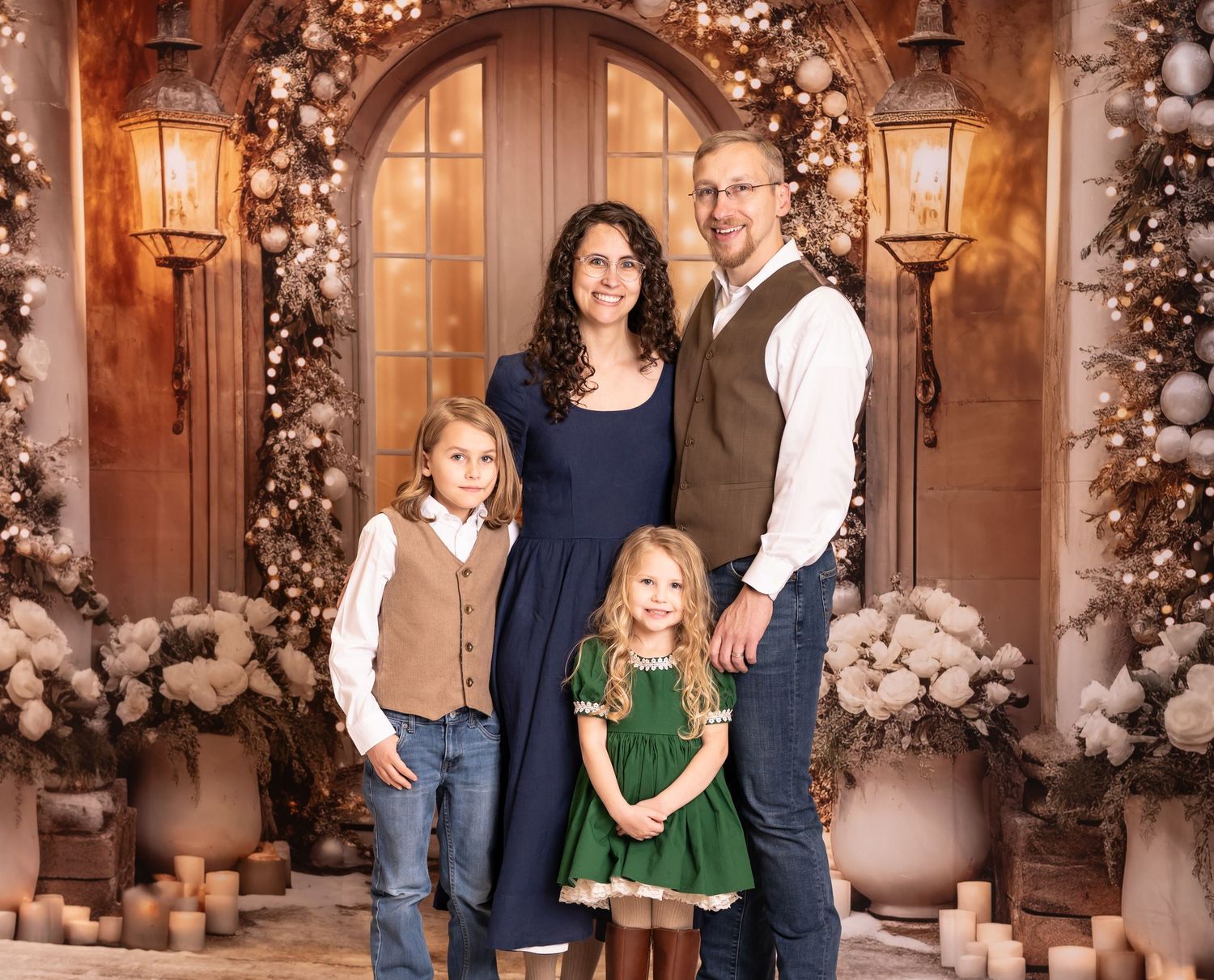 a family of four in jeans, vests and dresses poses in front of an elaborately decorated Christmas doorway with gold tones and florals