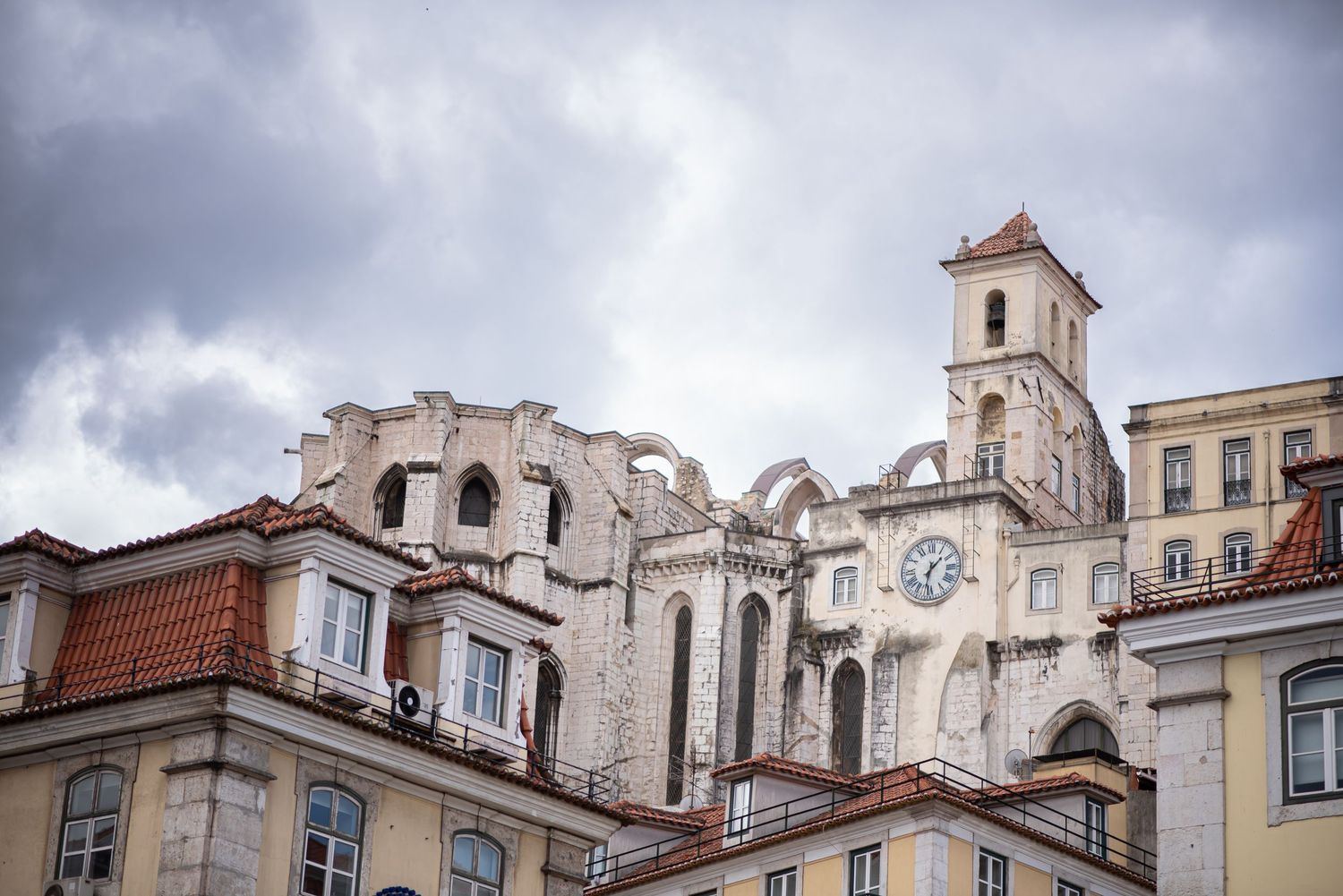 Historic ruins of Carmo Convent with clock tower in Lisbon, Portugal, under dramatic cloudy skies.