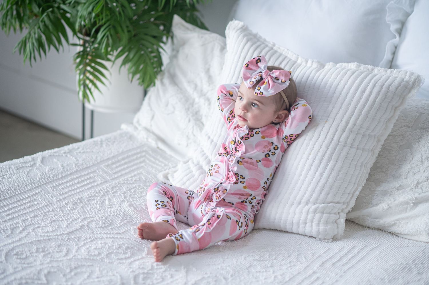 A baby girl models a pink floral zip-up romper and matching bow headband for a product shoot.