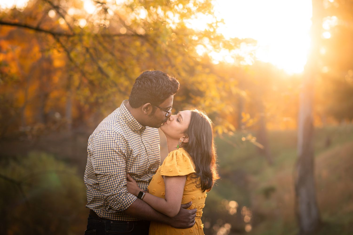 a sun-drenched golden hour portrait of an Indian couple standing in a meadow kissing