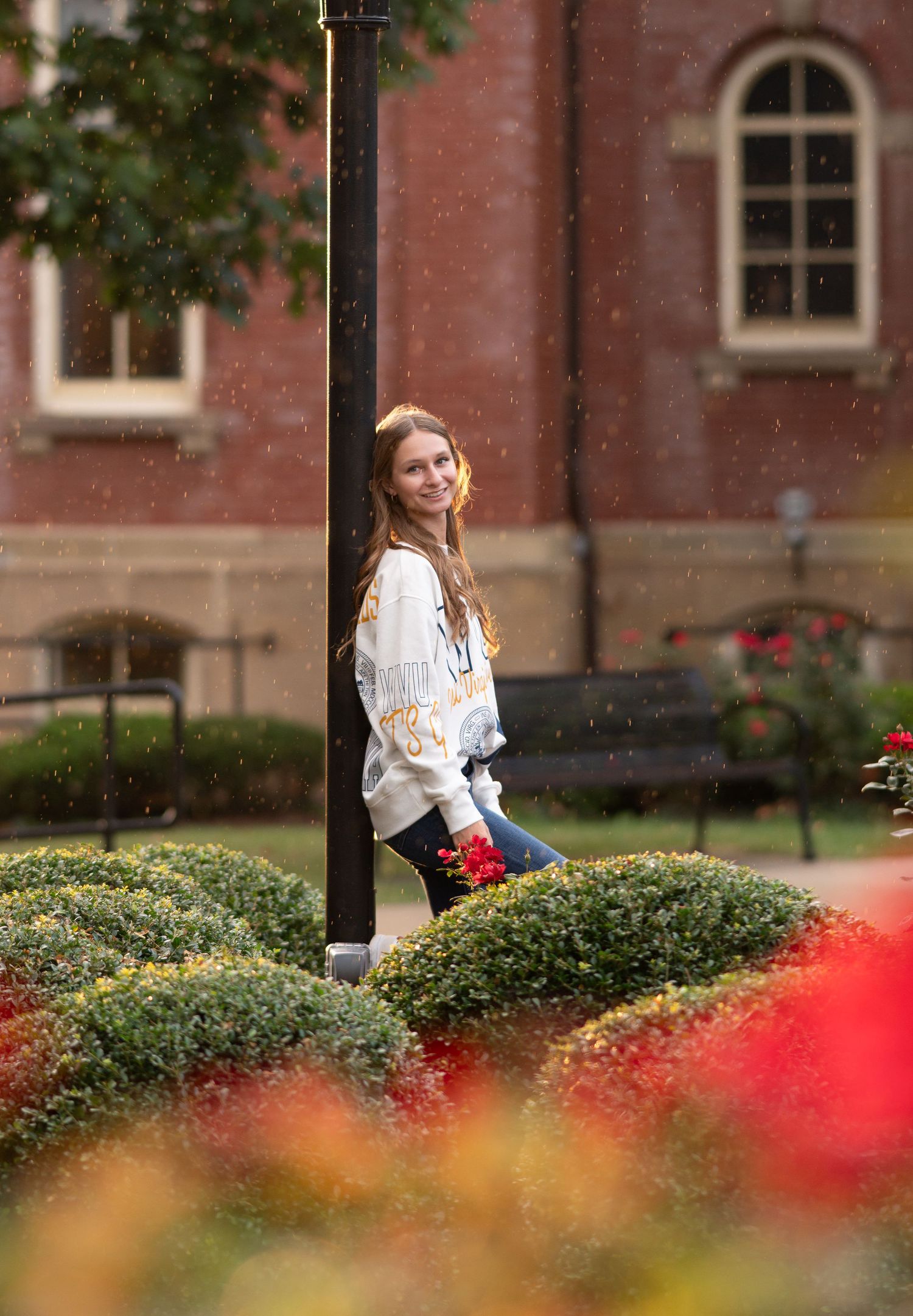 a high school senior leans against a lamp post on WVU's campus and poses for a senior portrait with roses all around