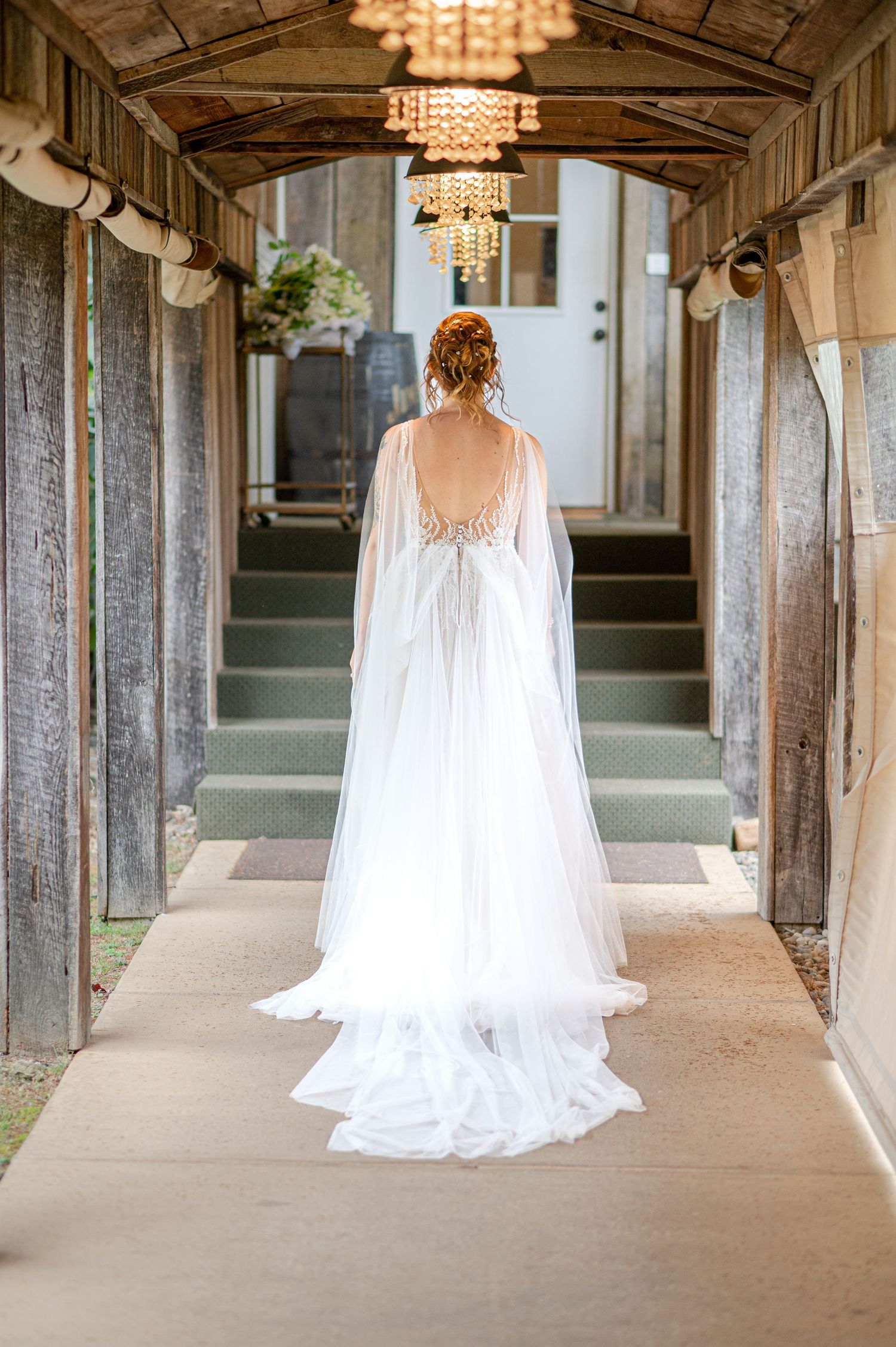 a bride in a white dress with a long white train walks away through a series of arches with chandeliers hanging overhead