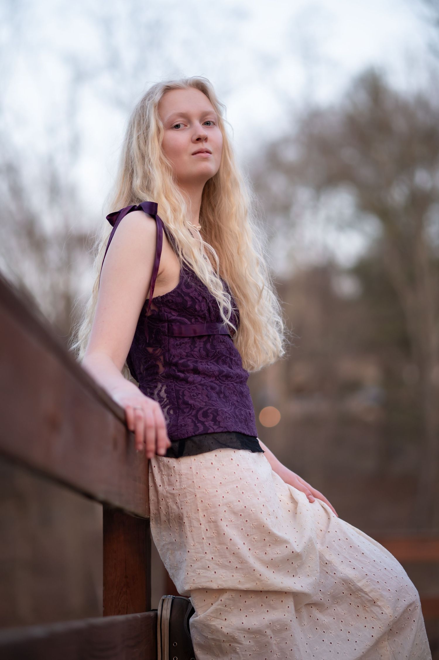 a young high school graduate with long blonde hair poses on a wood pier, looking down at the camera