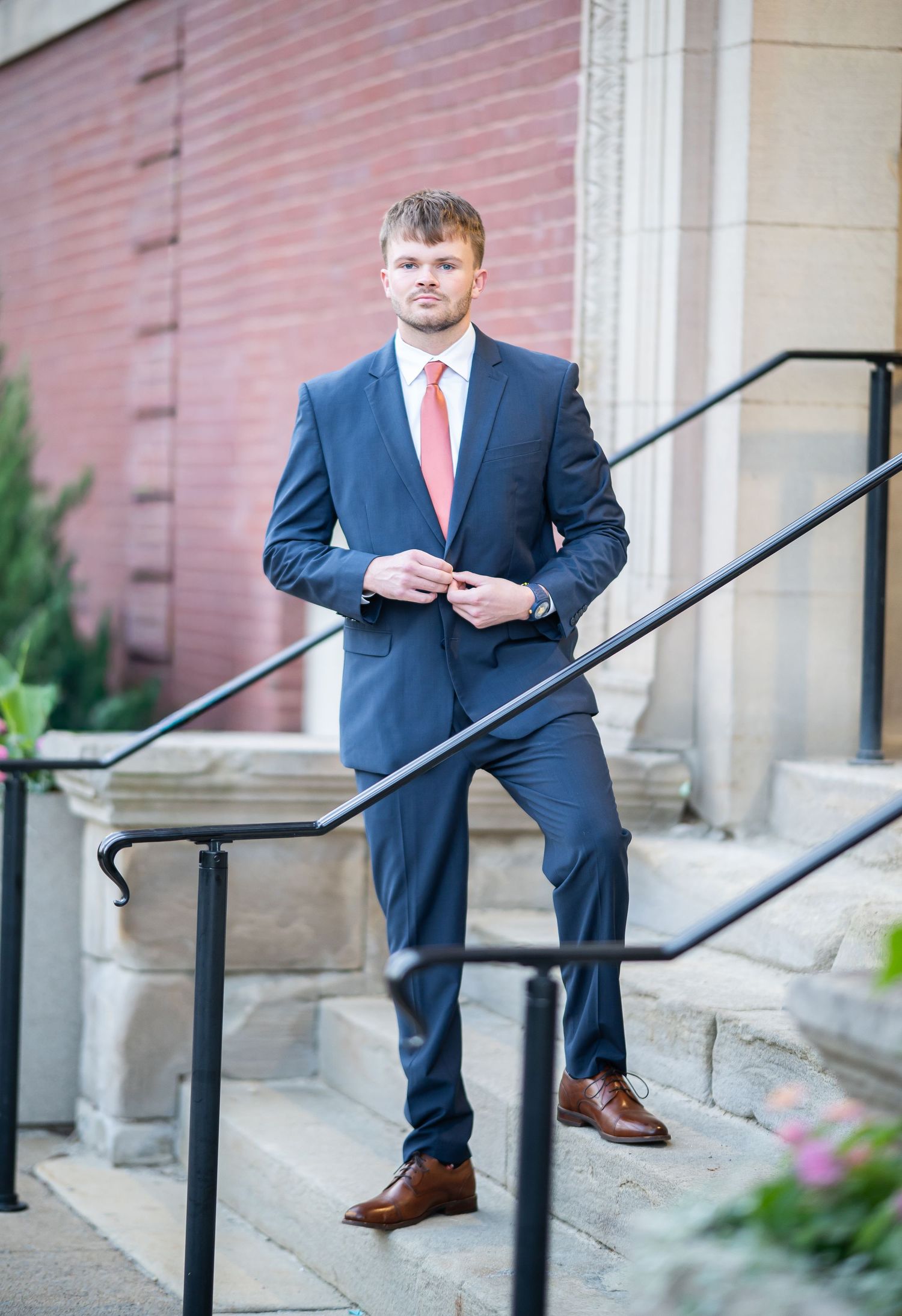 A WVU graduate in a blue suit and red tie poses for a portrait on the steps in Woodburn Circle in Morgantown, WV