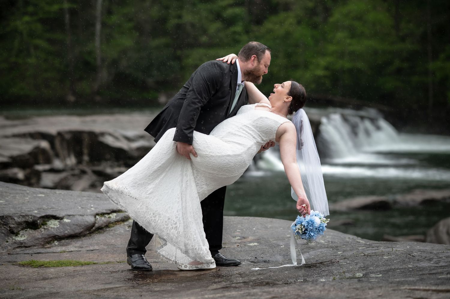a groom dips his bride in front of a waterfall in the rain, at Valley Falls, WV