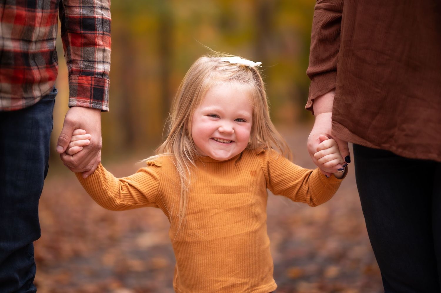 candid closeup of a sweet little blonde girl in a yellow sweater holding her parents hands and laughing into the camera
