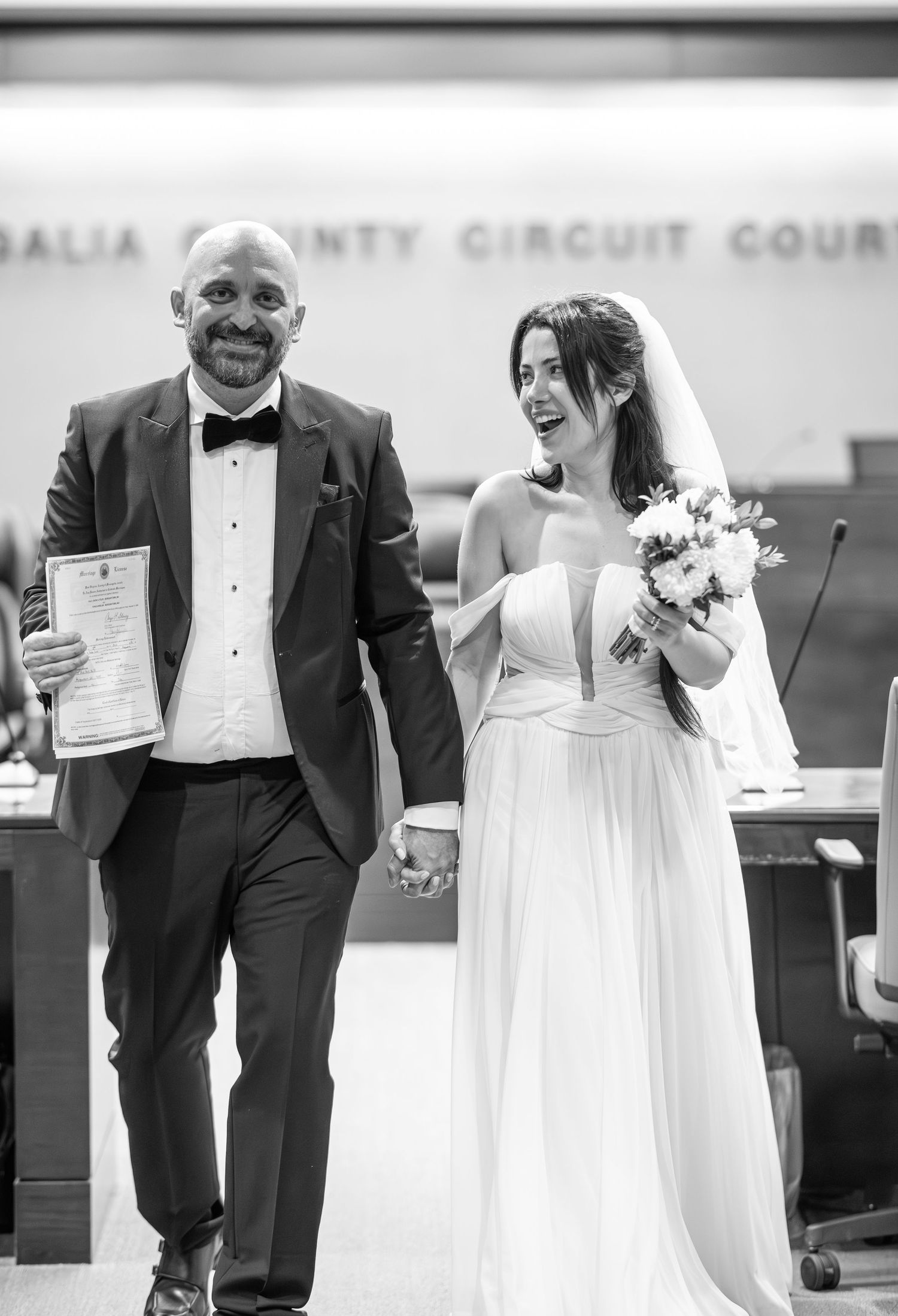 a bride and groom walk down the aisle of a courtroom in Morgantown after their wedding ceremony; he holds a completed wedding certificate