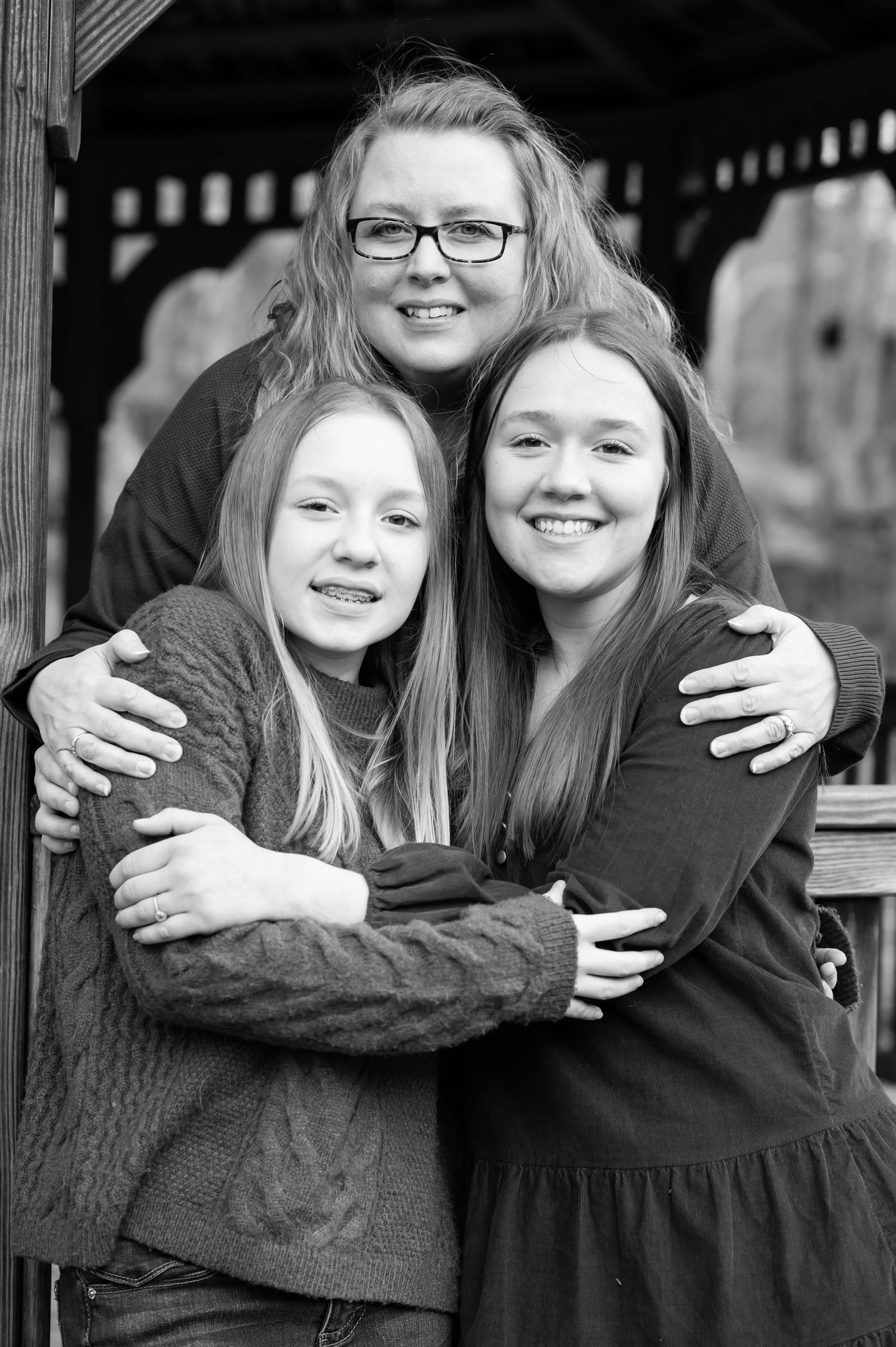 black and white portrait of a mother with her arms around her two teenage daughters, as all three smile for the camera