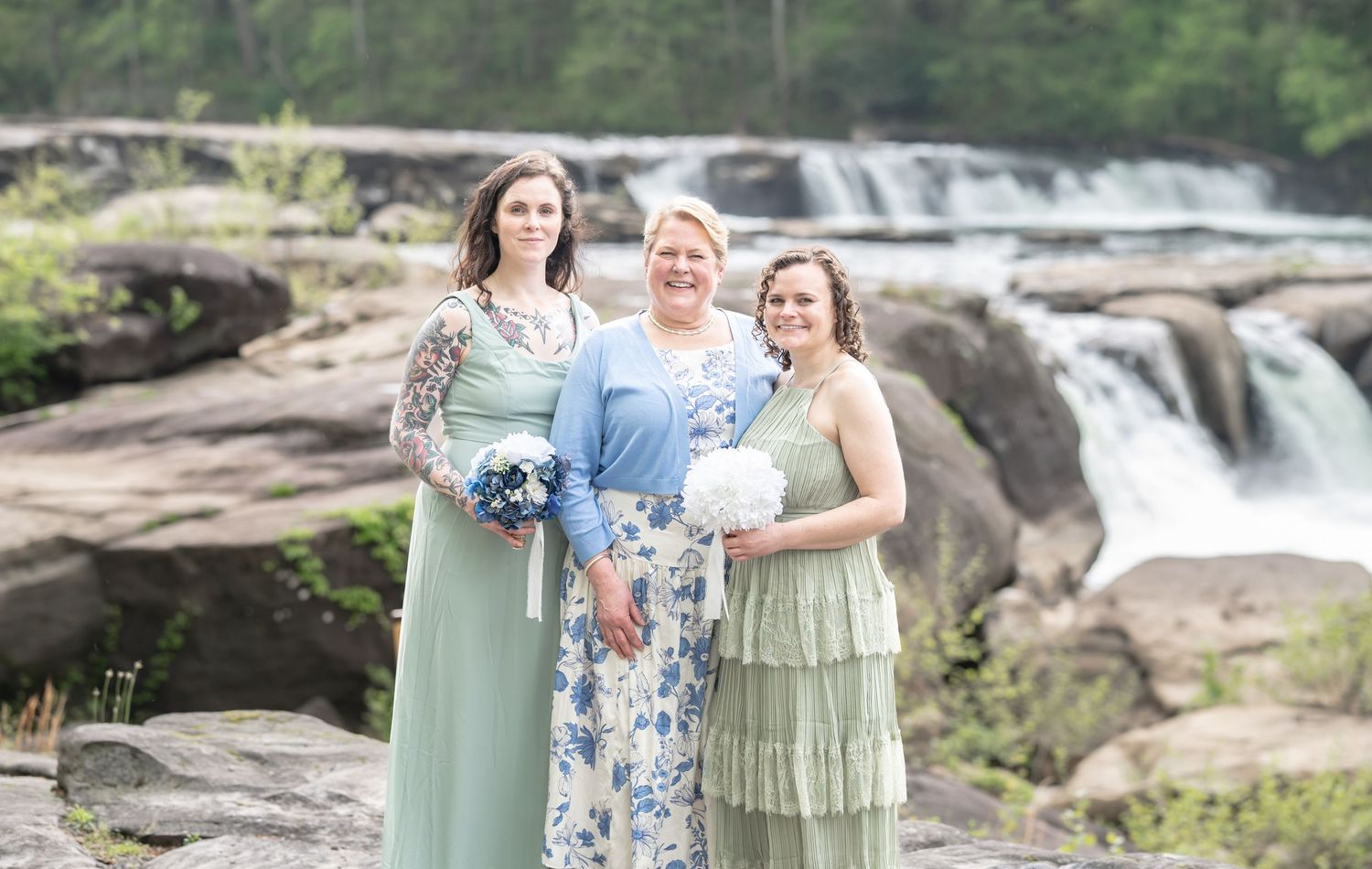 a mother of the groom and her two daughters in bridesmaid dresses pose together for a portrait with Valley Falls in the background