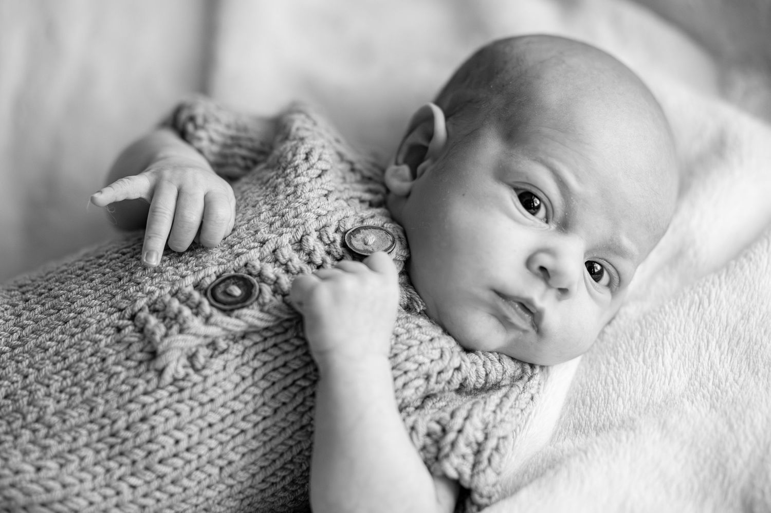 Black and white newborn baby wrapped in knit blanket lying down, looking alert and peaceful.